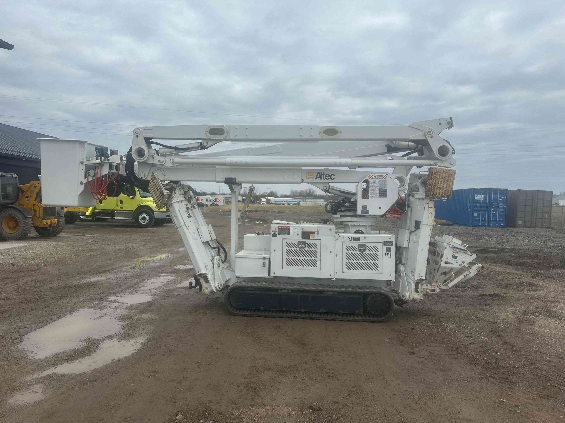 White tracked drilling rig on a muddy construction site under a cloudy sky