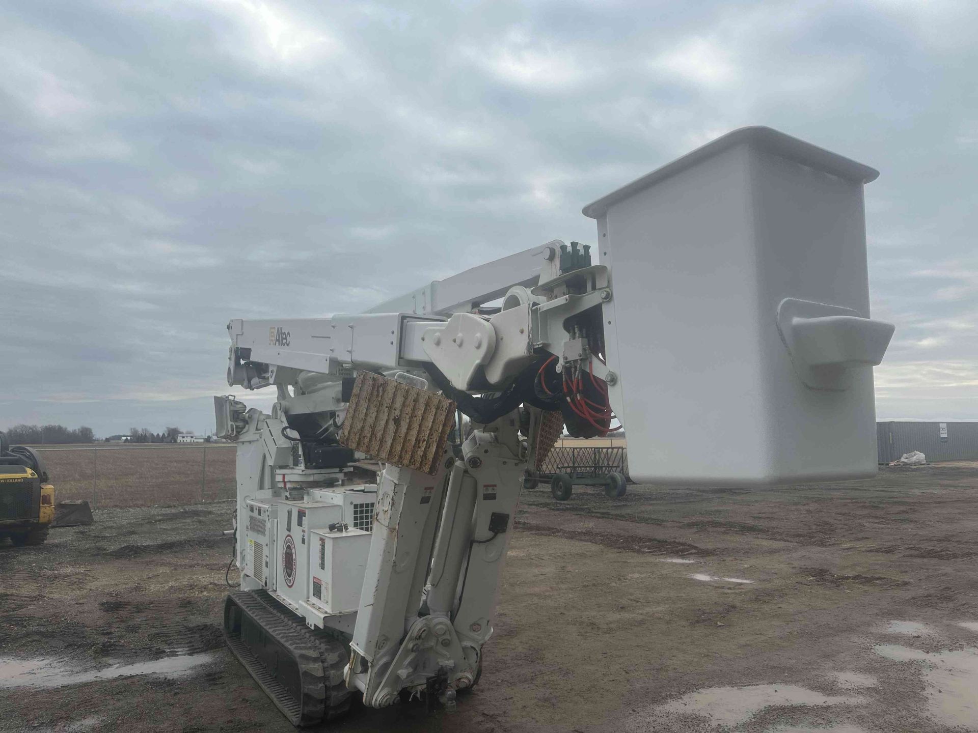 White tracked demolition machine lifting a large white structure in a muddy construction site under cloudy skies