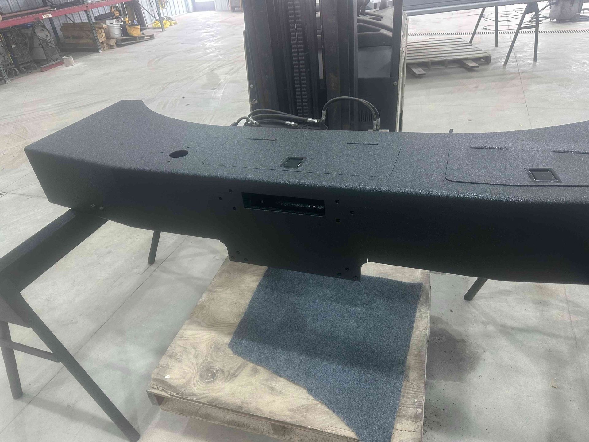 Black curved car body panel on a stand in a workshop, with a central grille opening.