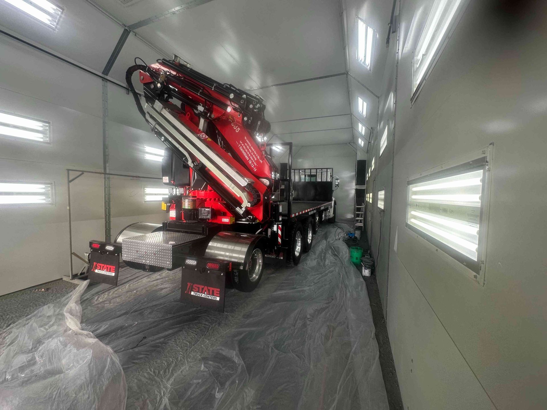Red crane truck parked inside a white spray booth, with plastic-covered floor and walls.