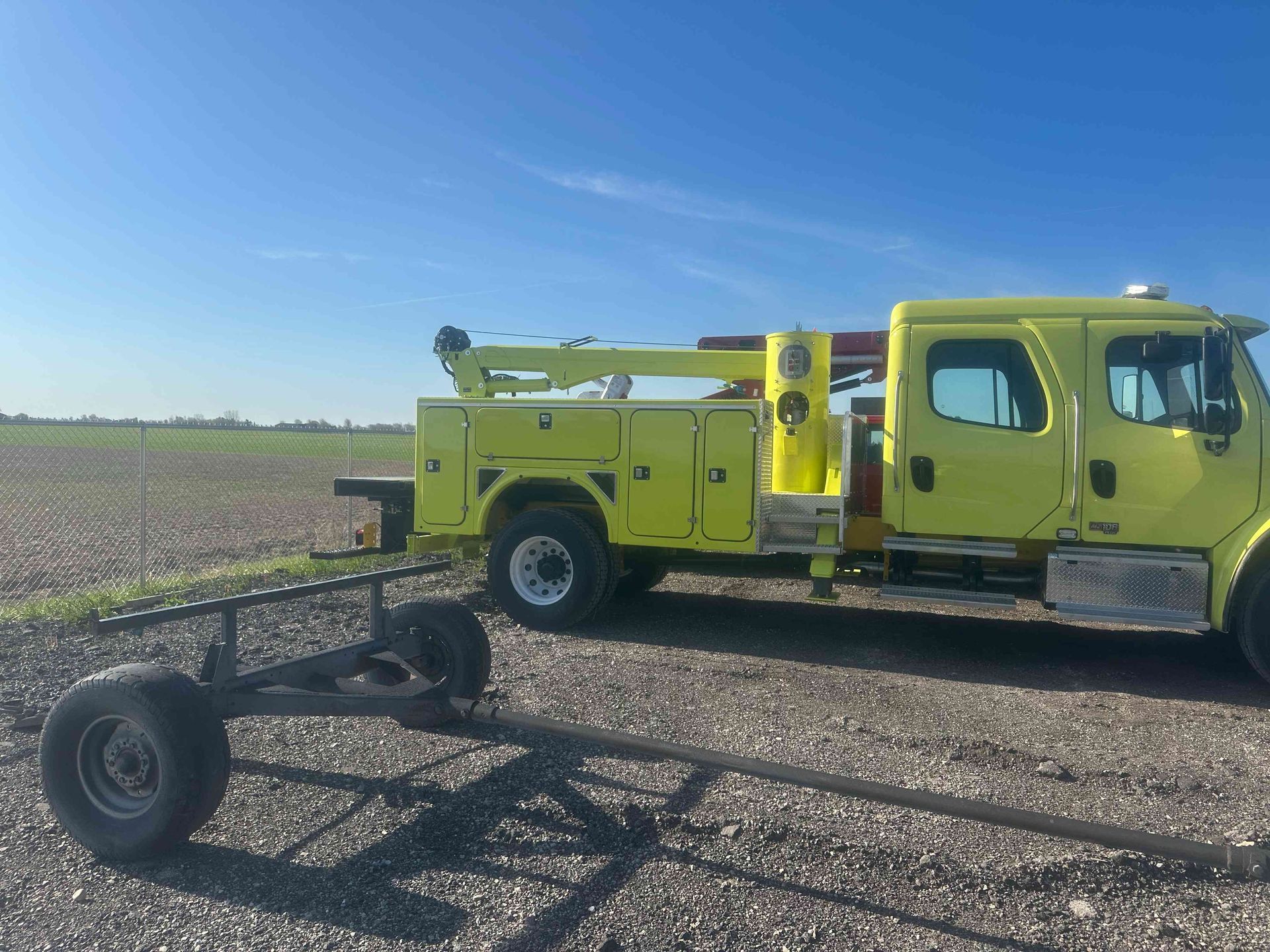 Yellow utility truck with trailer frame parked in a field under a blue sky