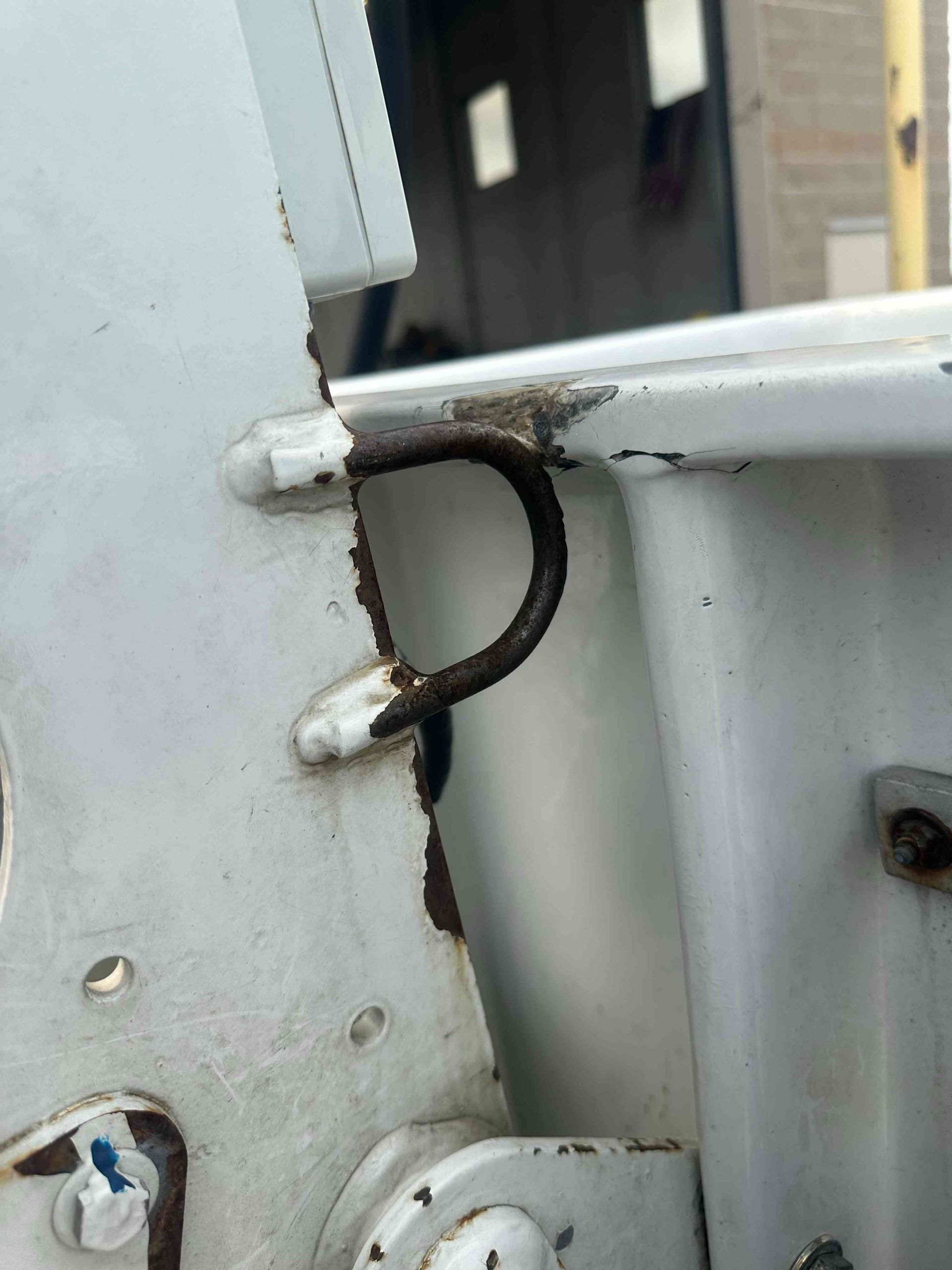 Close-up of a black looped strap attached to a light gray metal hinge on a white panel