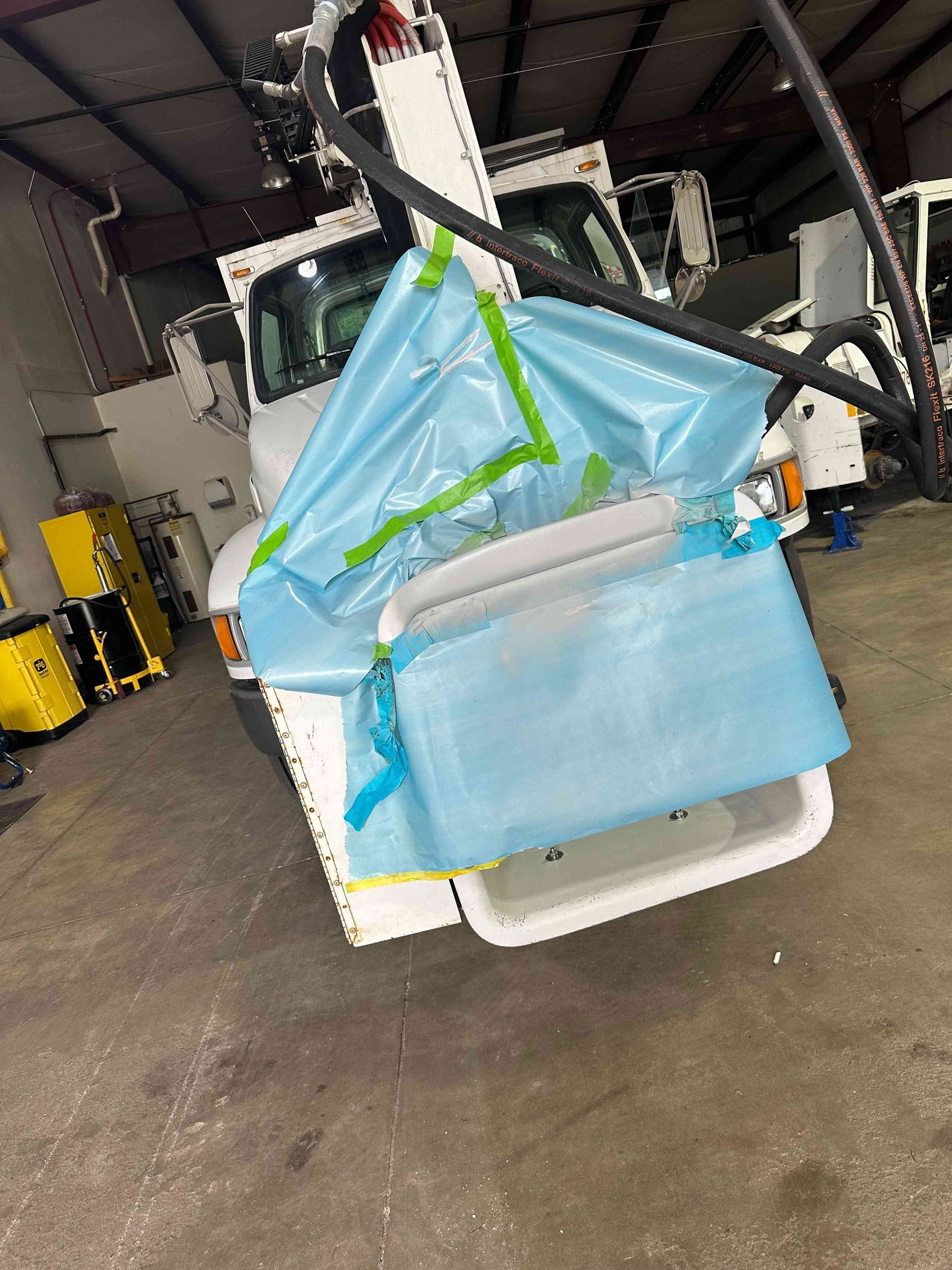 Damaged vehicle front covered with blue tarp and green straps inside a warehouse garage