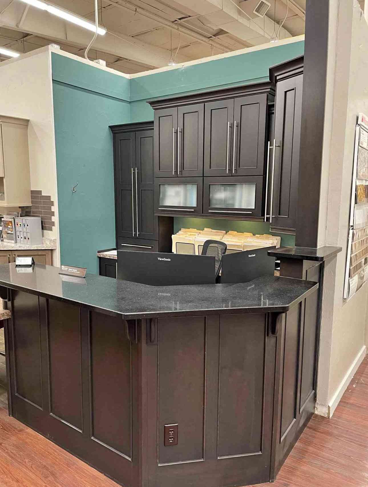 Dark wood kitchen island with black countertop and cabinets in a showroom with teal walls