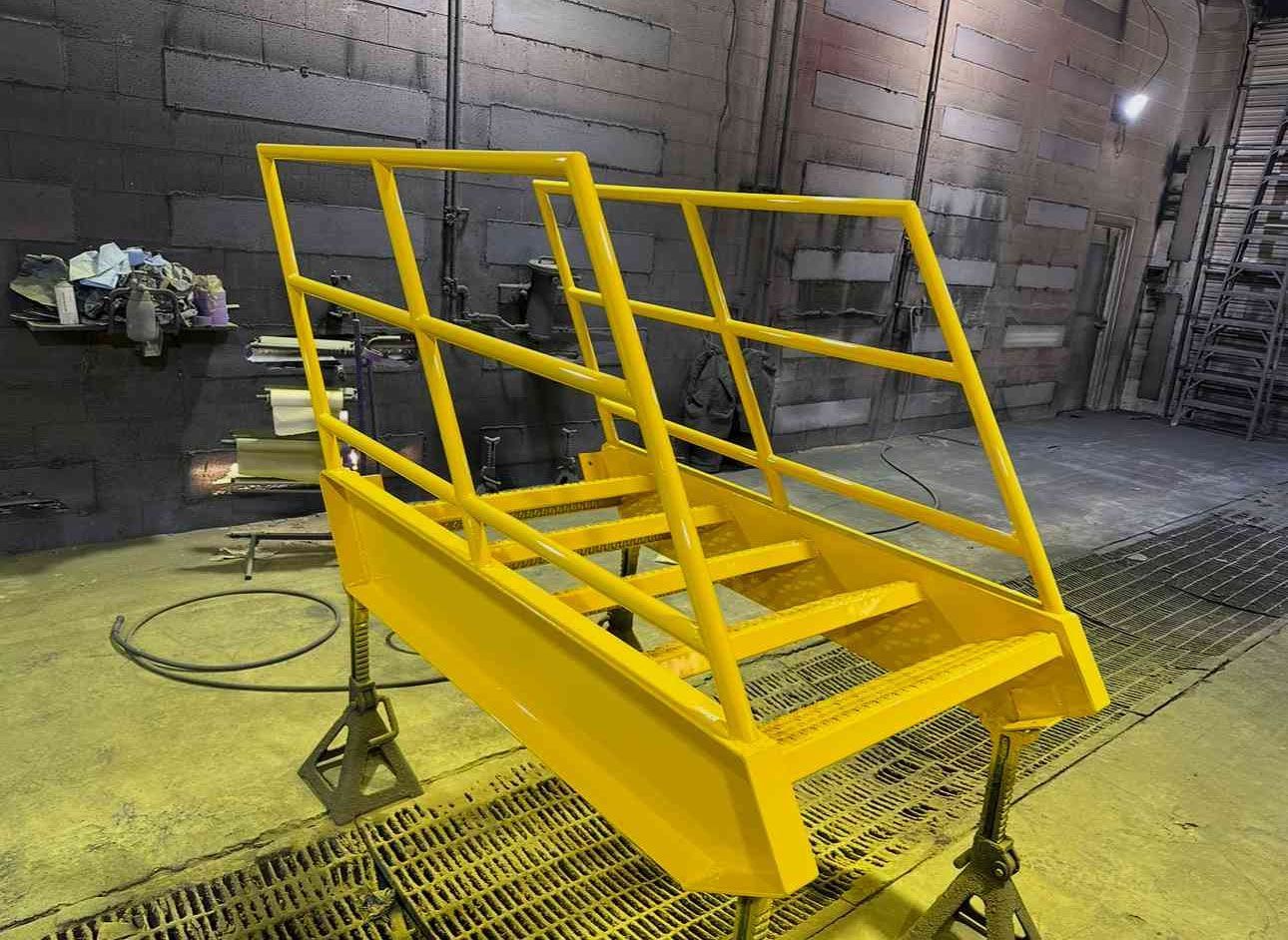Yellow metal platform with handrails in an industrial workshop, mounted on a wheeled base