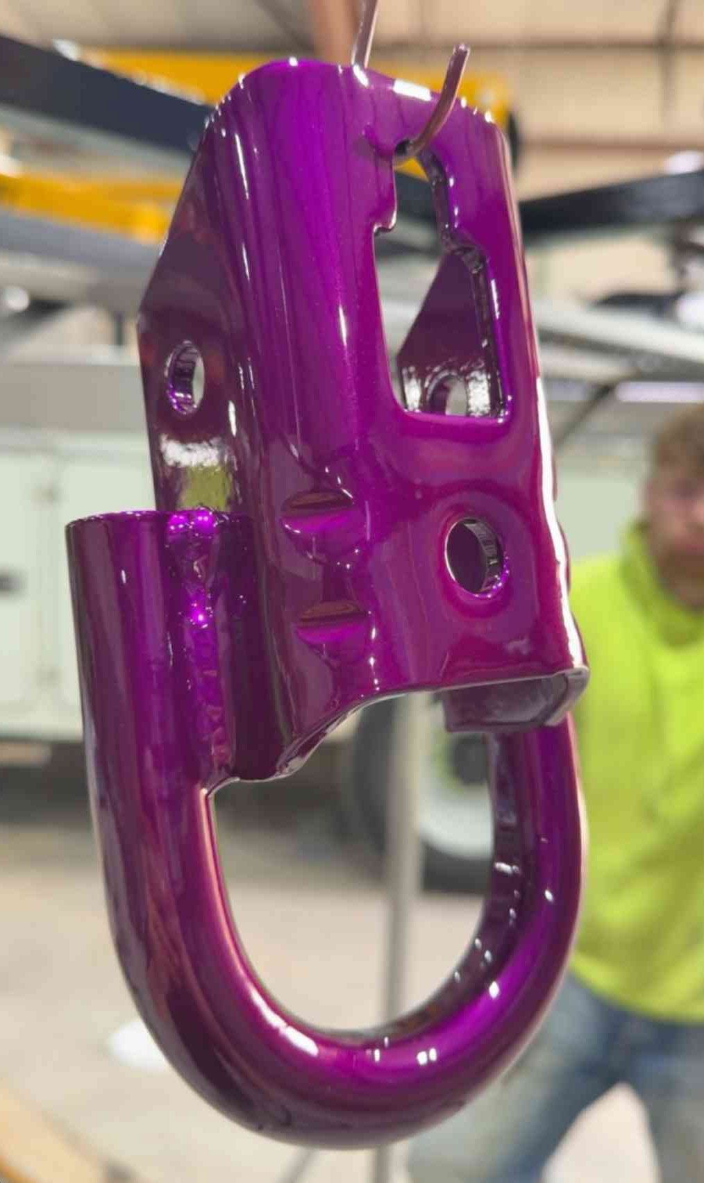 Purple metal hook latch hanging in a workshop, with a person blurred in the background