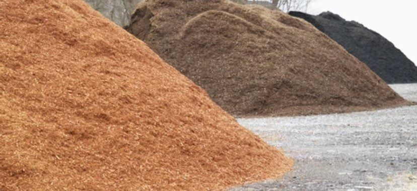 Large piles of orange and brown wood chips beside a gravel road