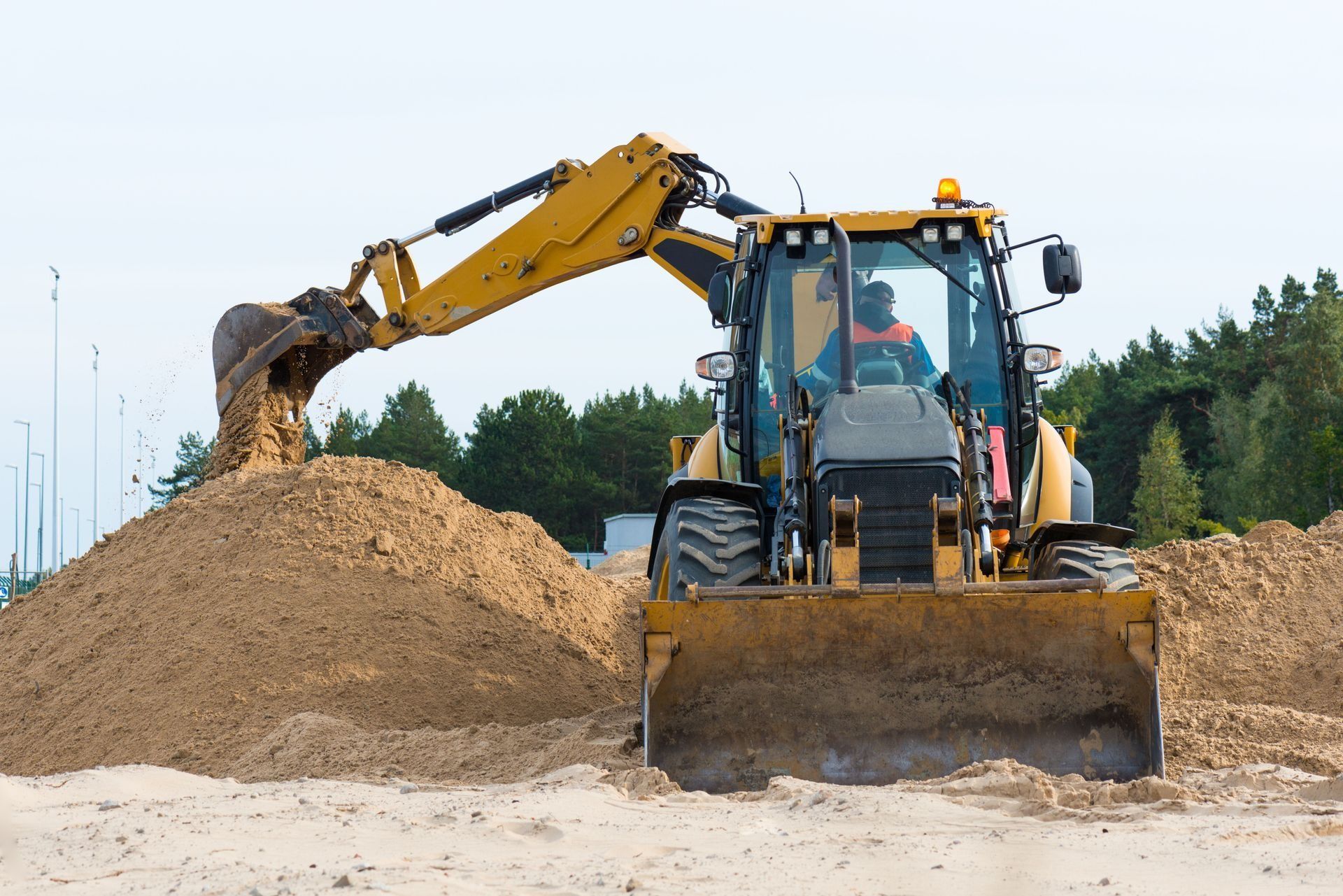 Yellow excavator loading sand at a construction site under a clear sky
