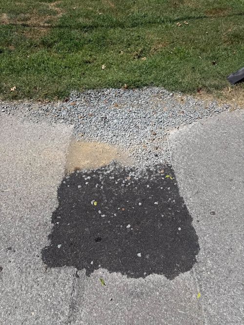 Patchy asphalt repair on a gray driveway beside grass and gravel.