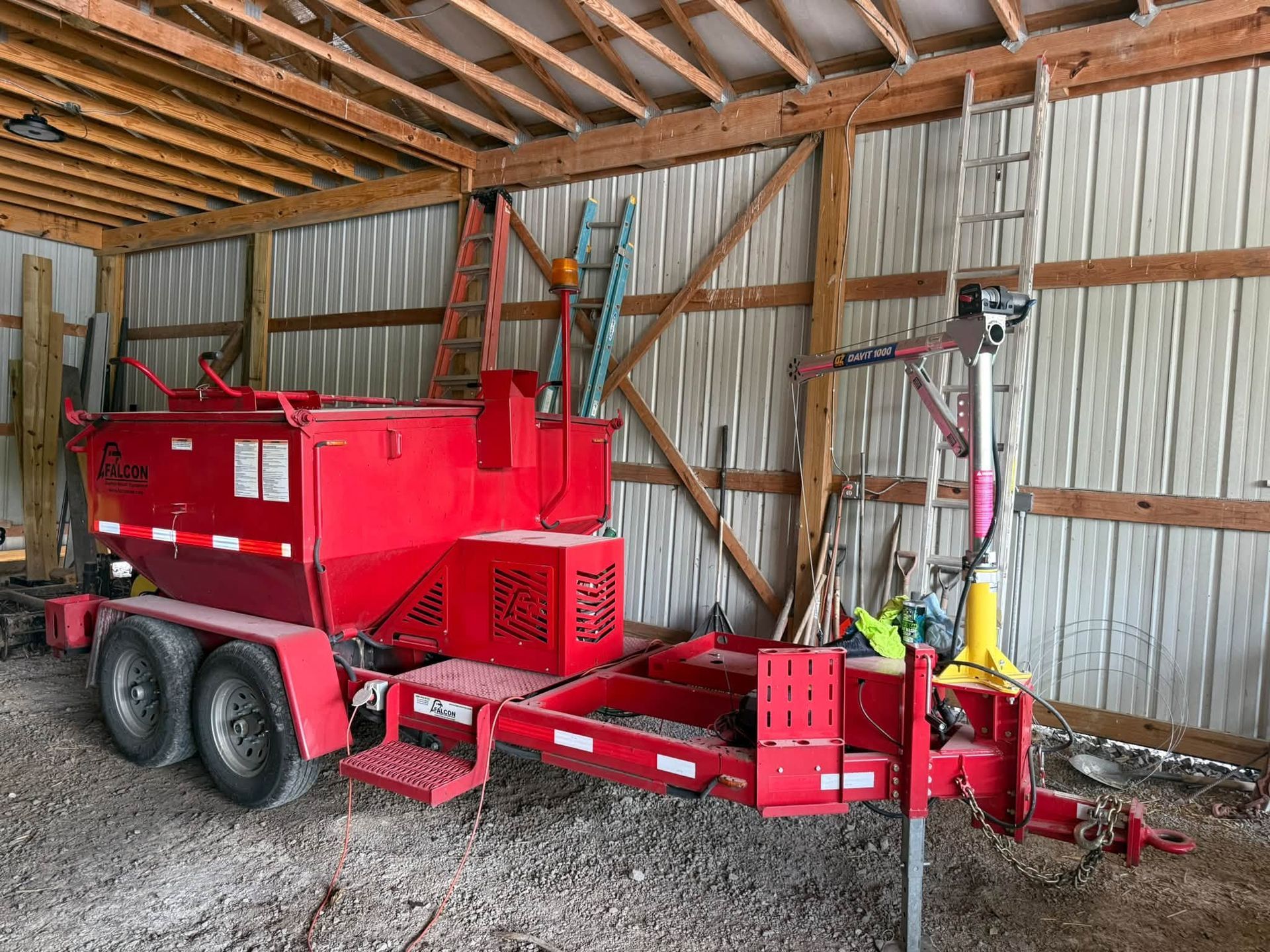 Red industrial wood splitter trailer parked inside a wooden barn.