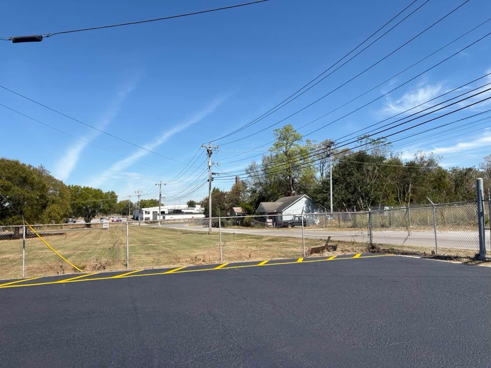 Empty asphalt lot behind a chain-link fence under a blue sky