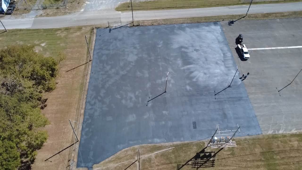 Aerial view of a freshly coated blue-gray basketball court with one person near the right side.