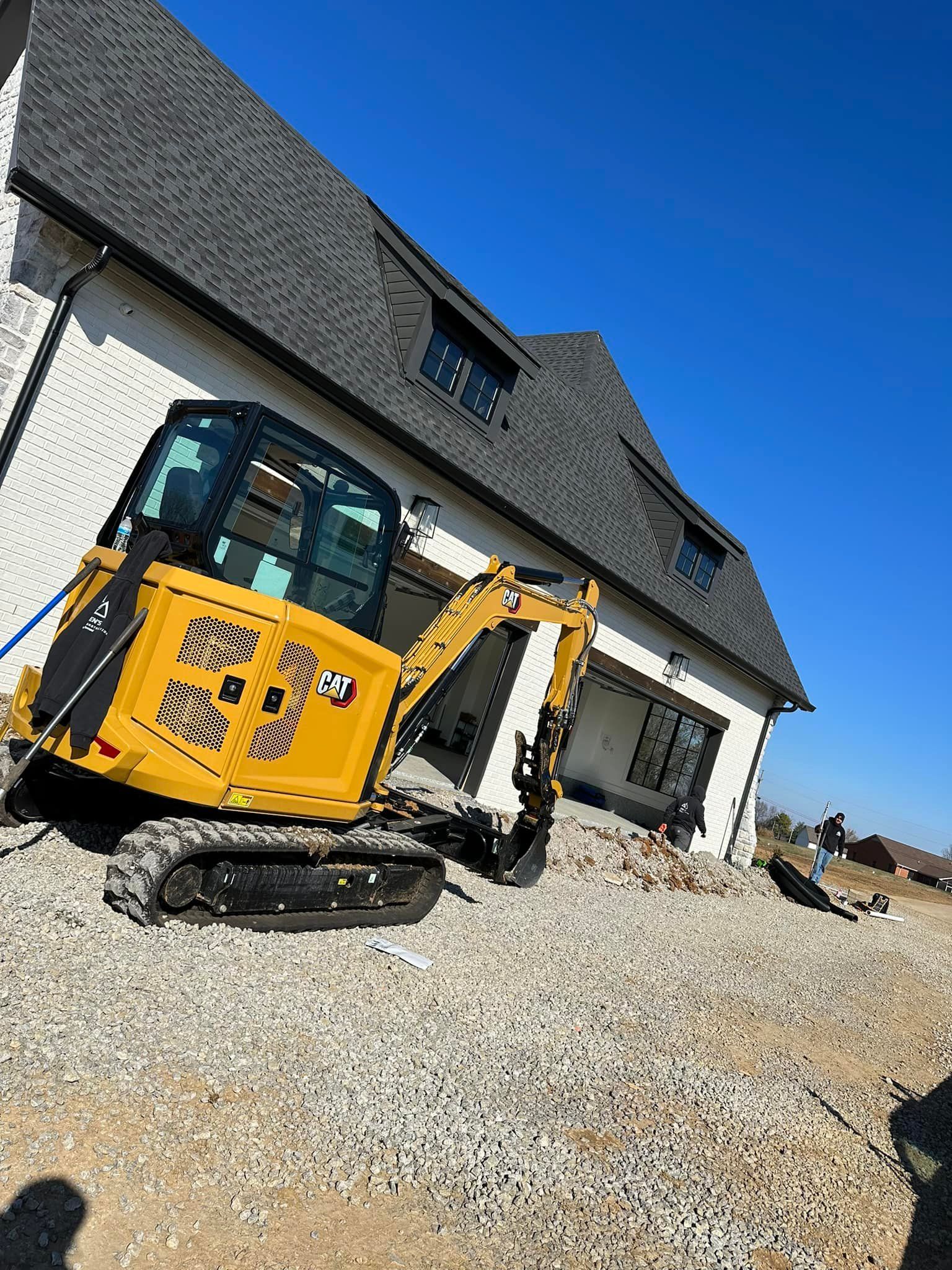 Yellow mini excavator on gravel next to a two-story house under construction. Blue sky.
