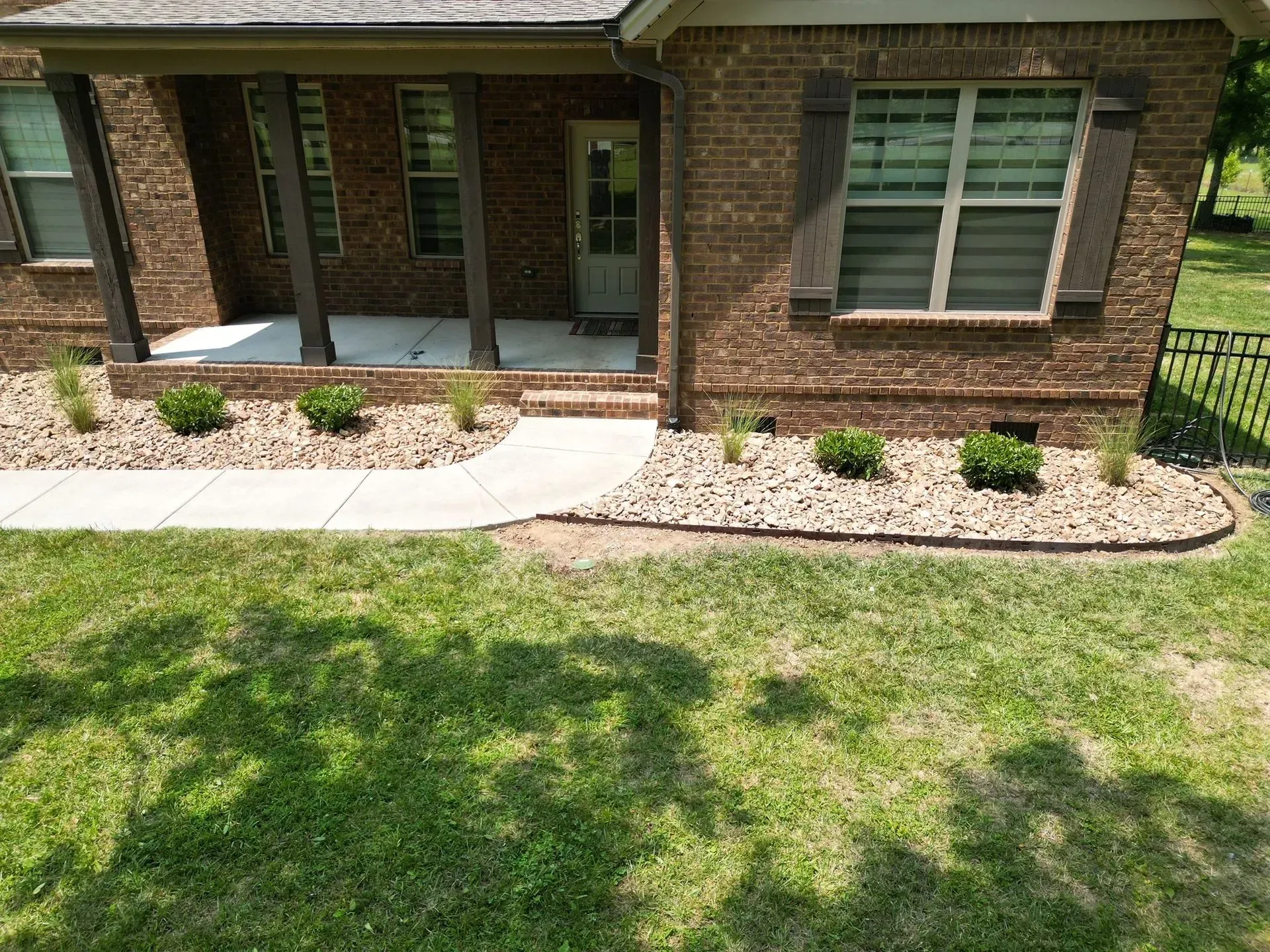 Brick house with concrete path, mulch beds, and green shrubs.