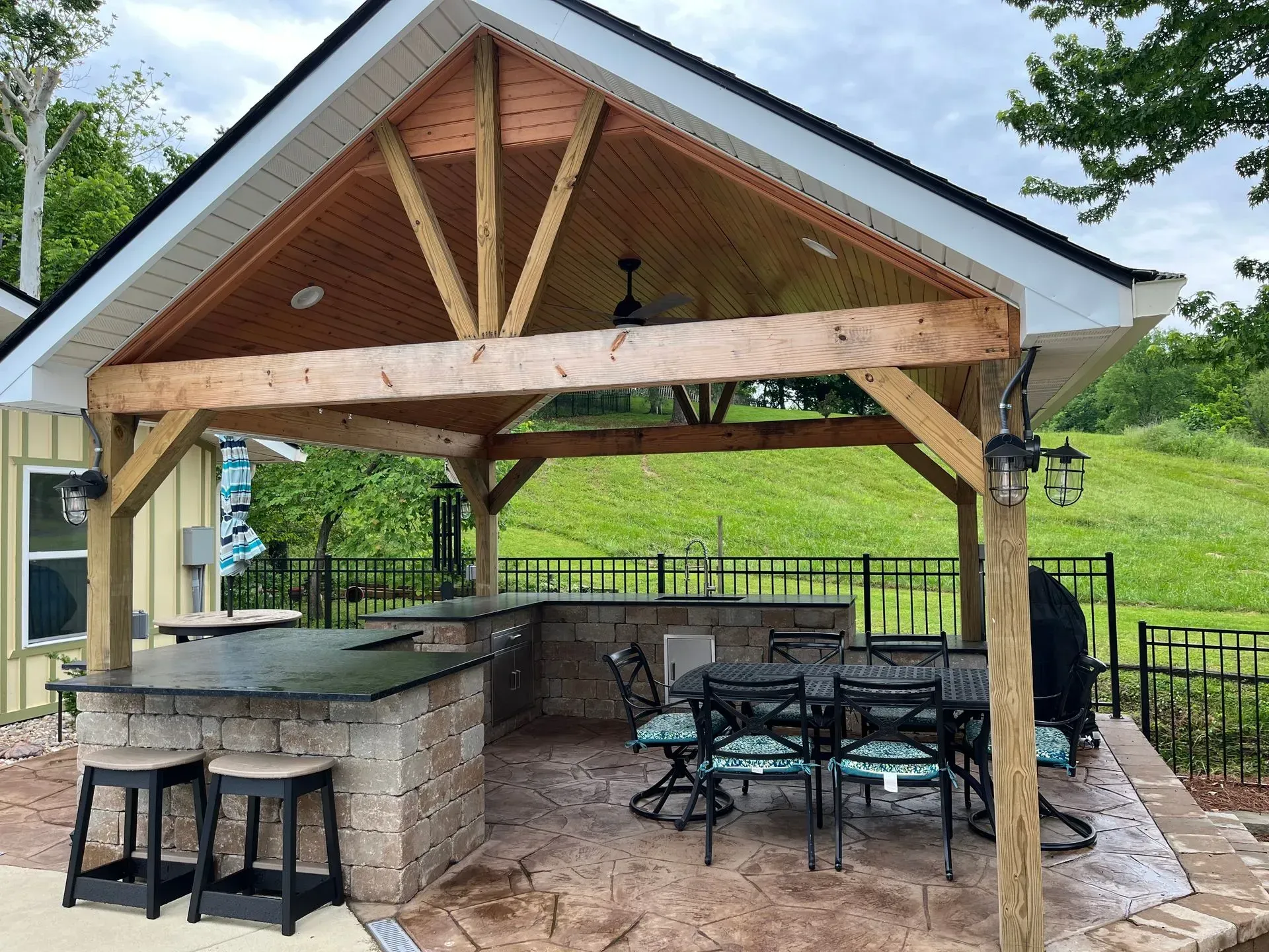 Outdoor kitchen with stone bar, seating, grill, and a wooden pergola.