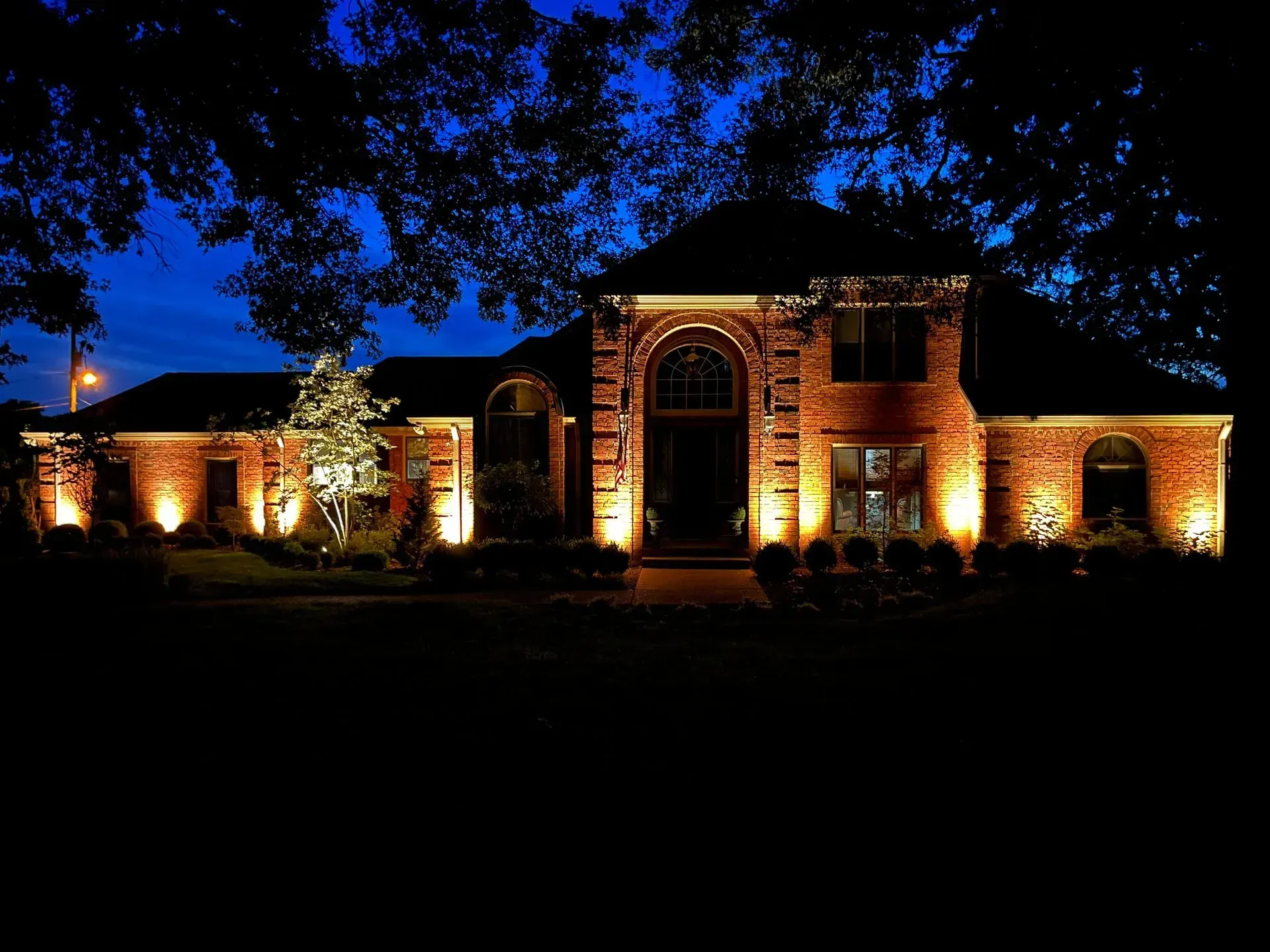 Brick house at night with golden uplighting. Blue sky in the background.
