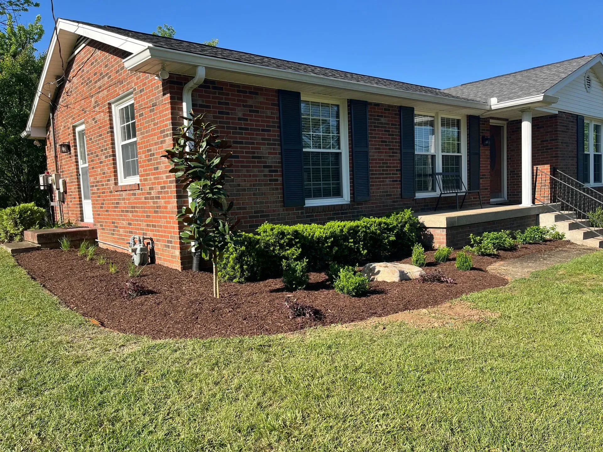 Brick house with blue shutters, lush landscaping, and a green lawn.
