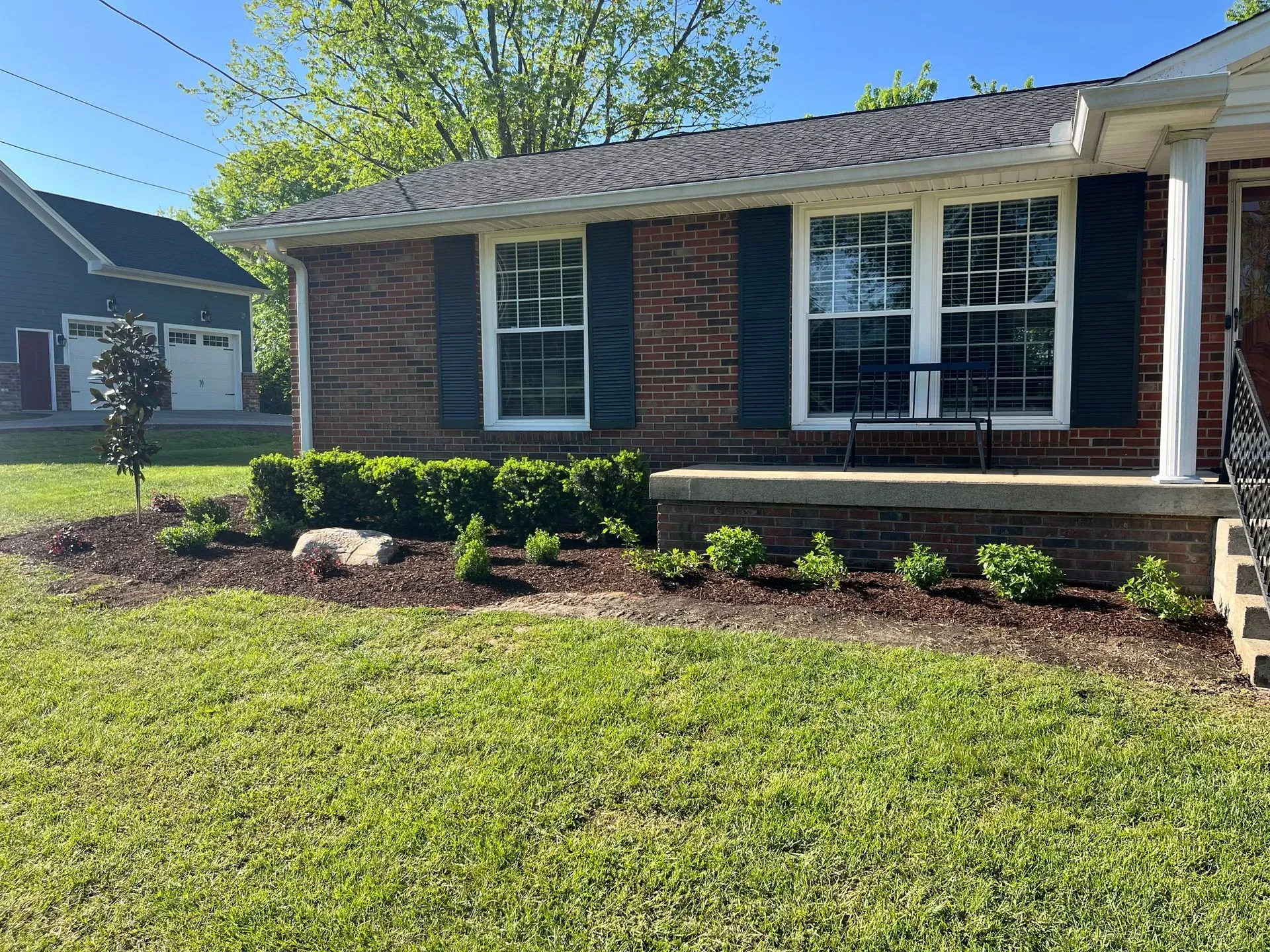 Brick house with manicured lawn and front flowerbeds, green grass, and blue shutters.