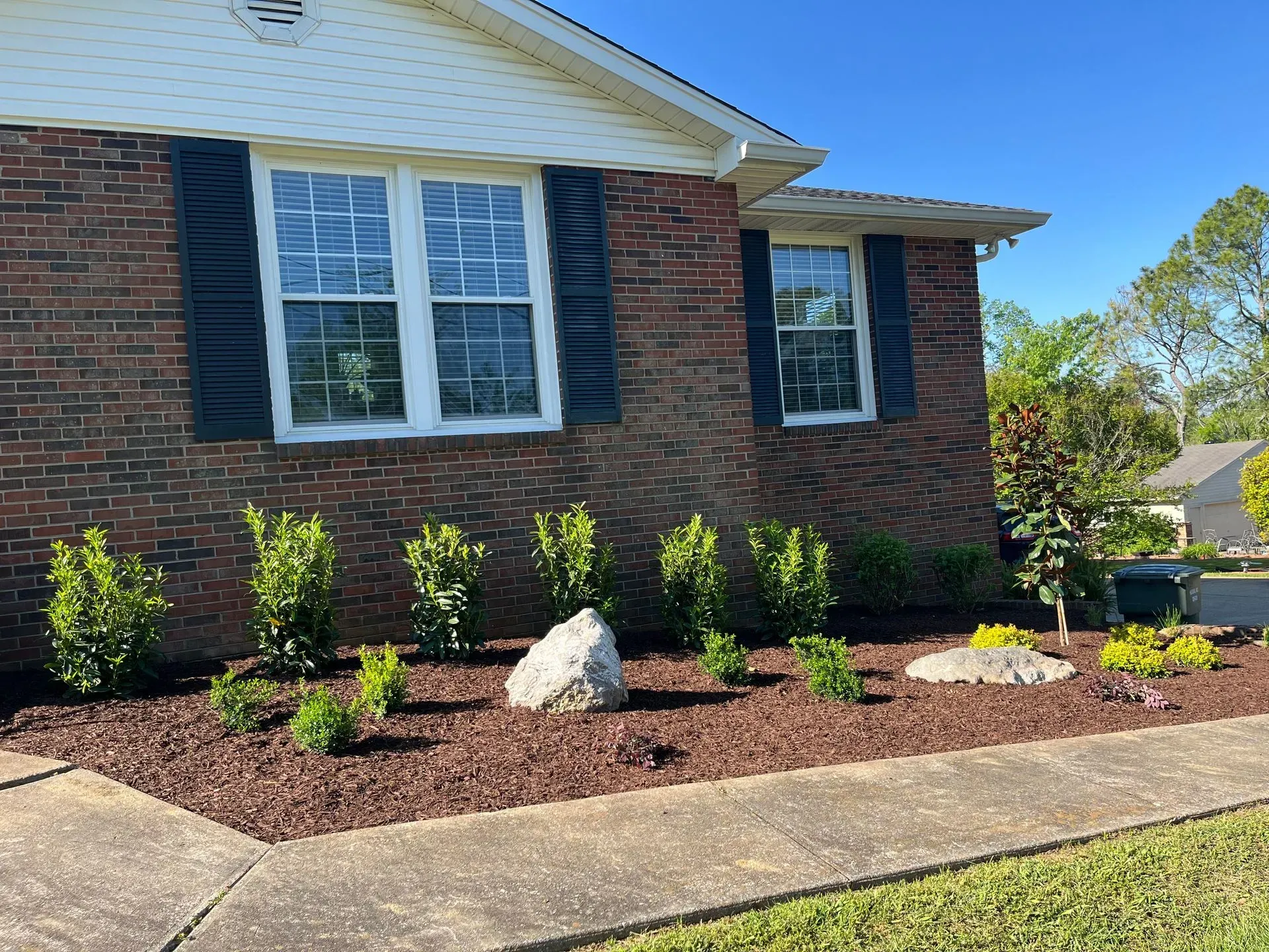 Brick house with manicured landscaping, including dark mulch, shrubs, and decorative rocks.