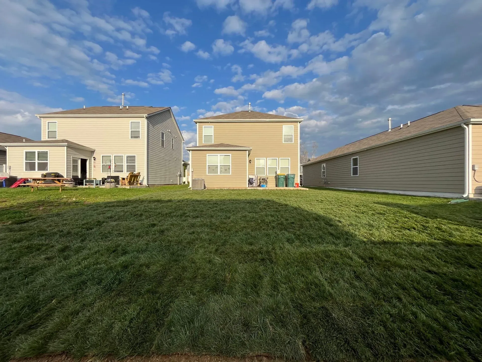 Backyards of beige houses under a blue sky, with green grass in between.