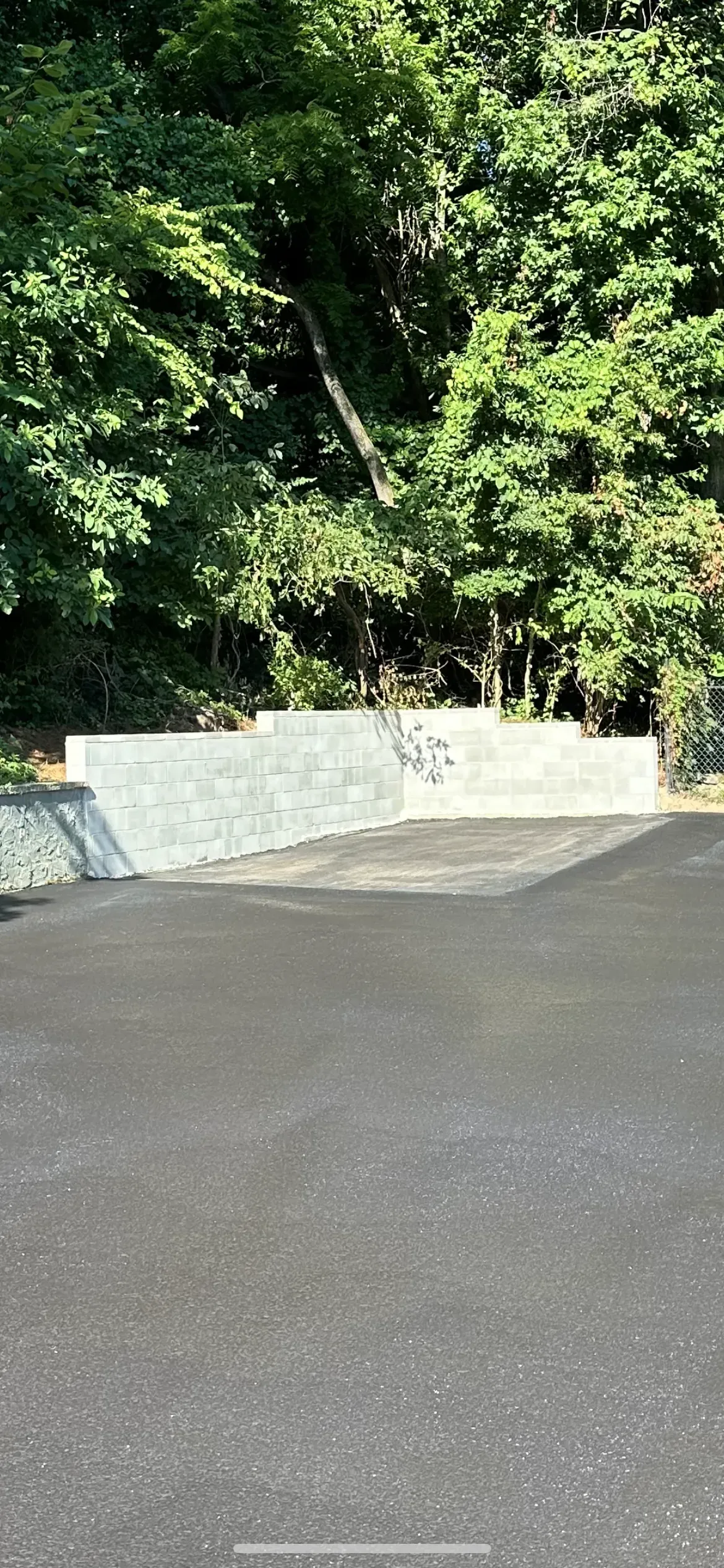 Asphalt road leads to a concrete barrier with trees in the background.