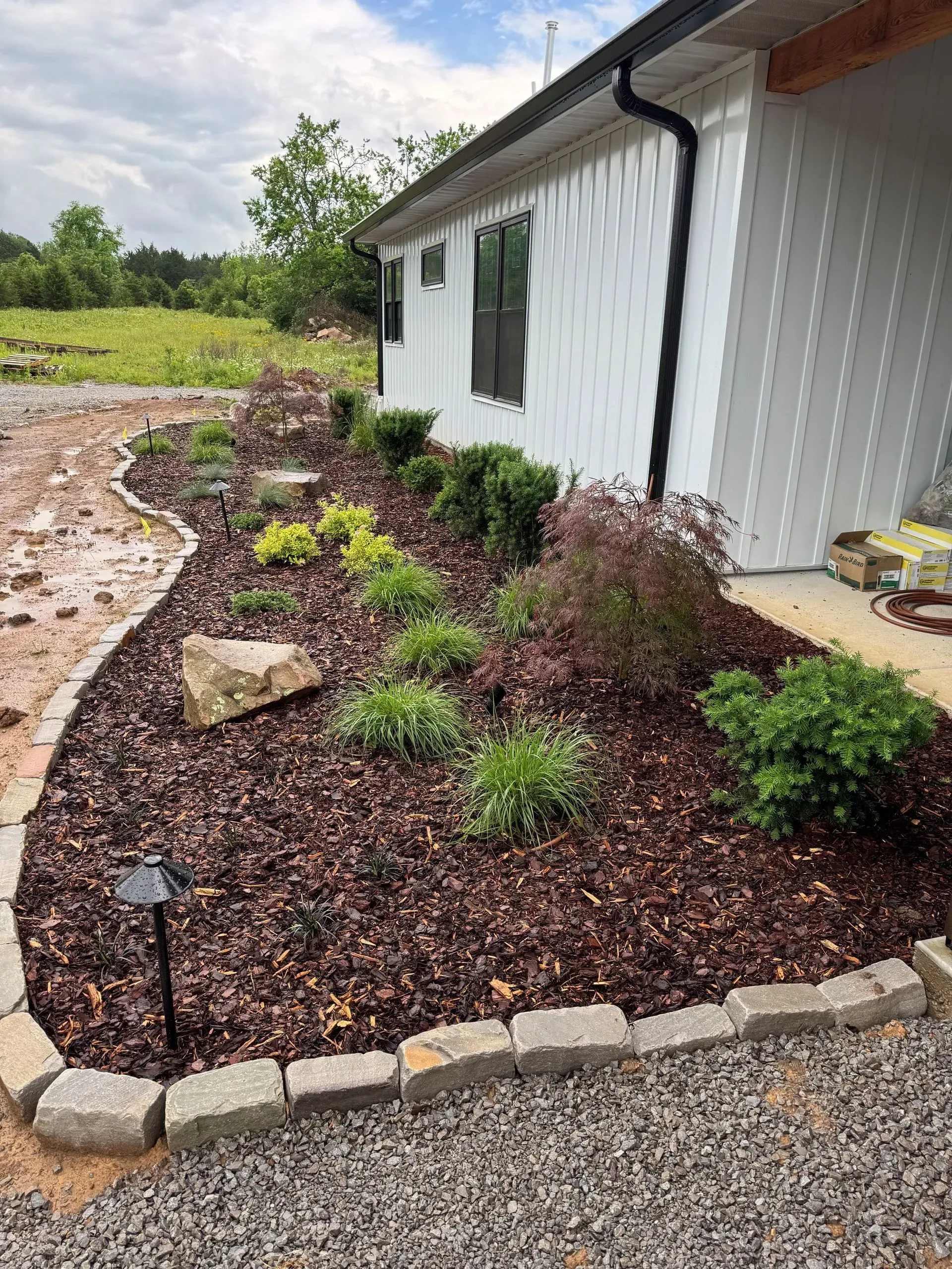 Landscaped flower bed with mulch, bordering a white house and gravel path.