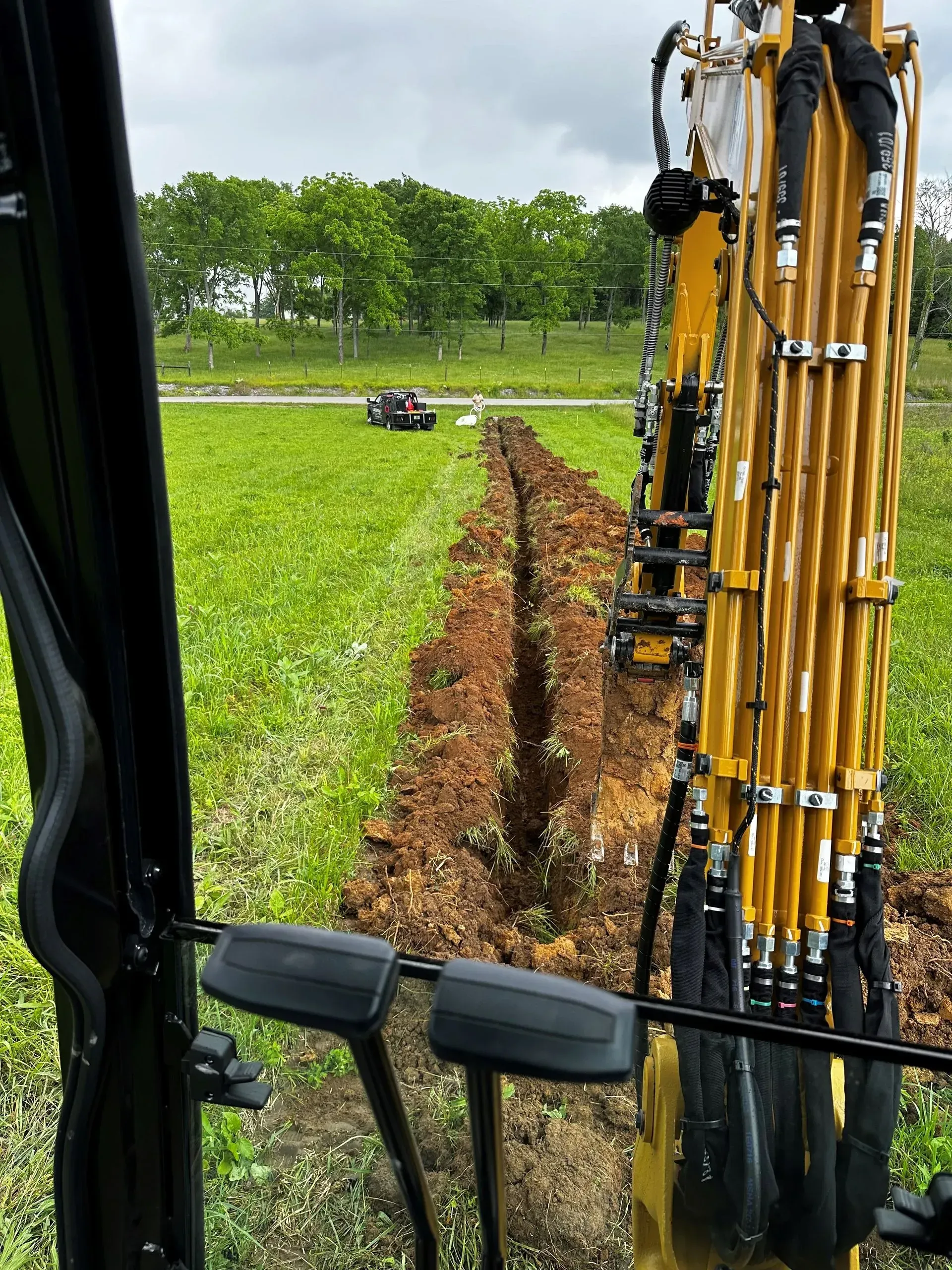 An excavator digging a trench in a grassy field; seen from inside the cab.