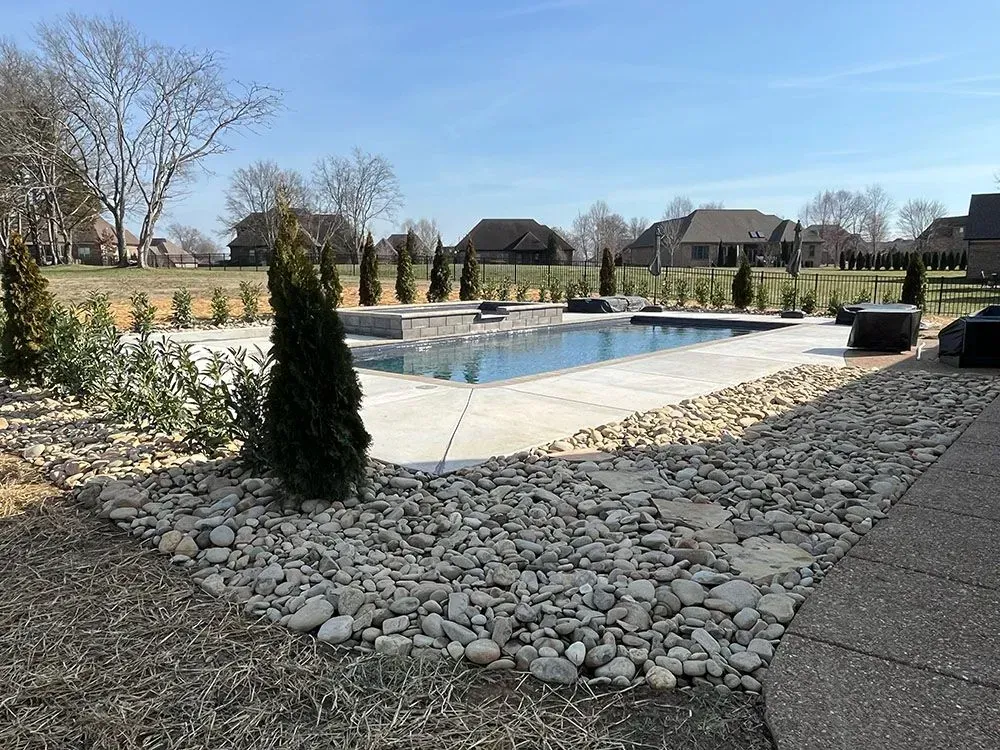 A rectangular pool surrounded by rocks and landscaping, under a blue sky.