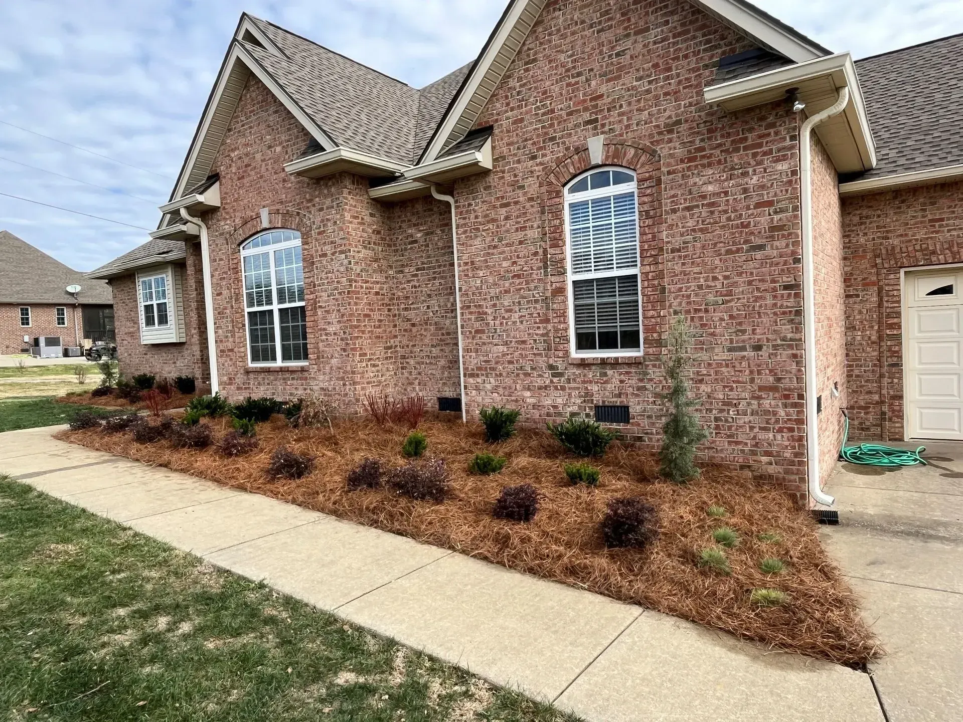 Red brick house with flowerbeds and tan mulch along a concrete path.