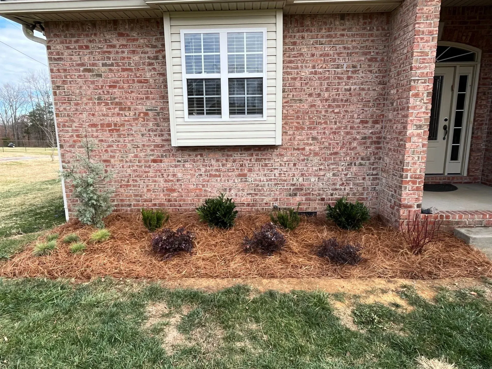 Brick house exterior with a small garden bed in front, featuring shrubs and mulch.