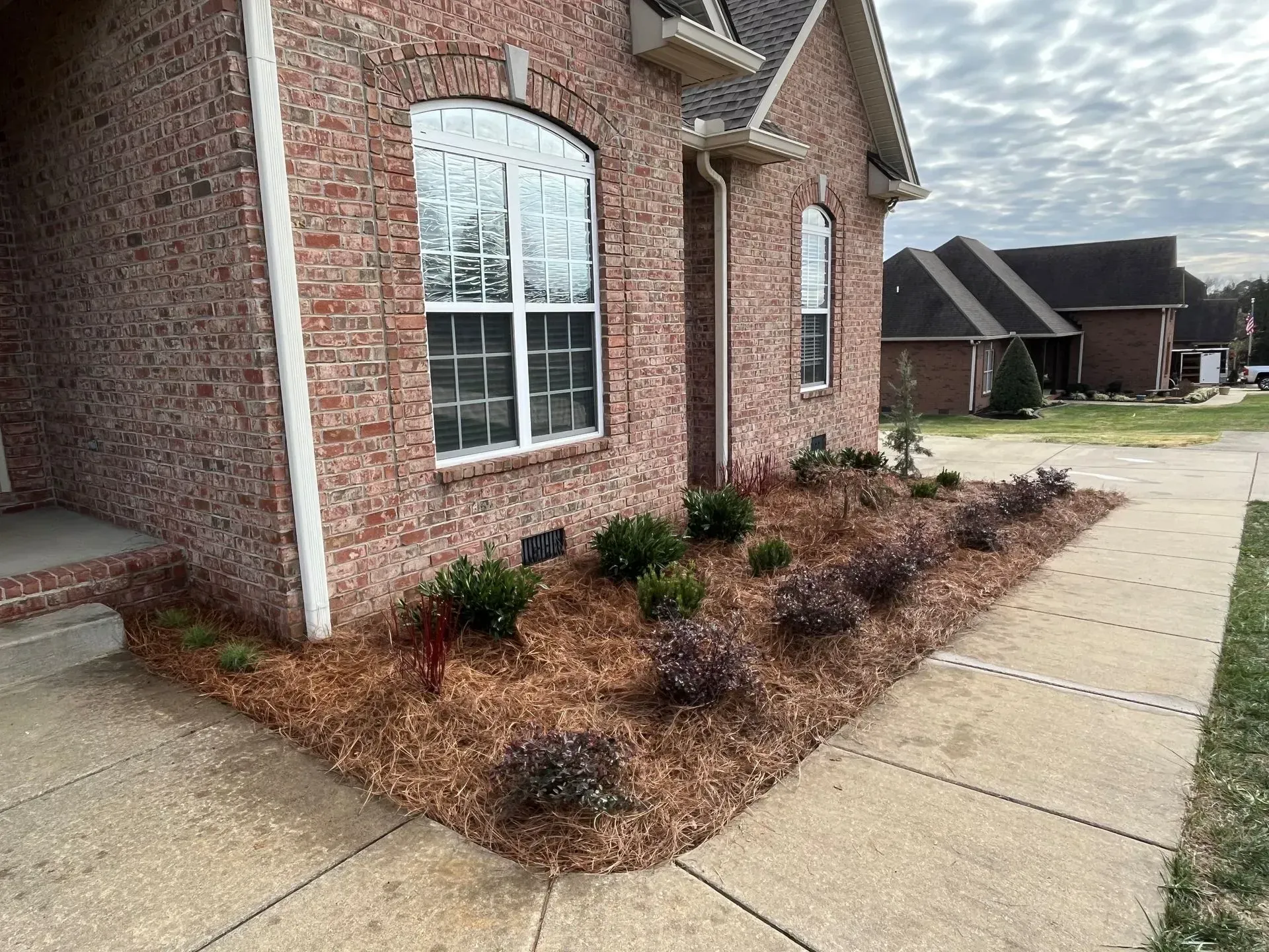 Brick house exterior with a landscaped garden bed, mulch, and bushes.