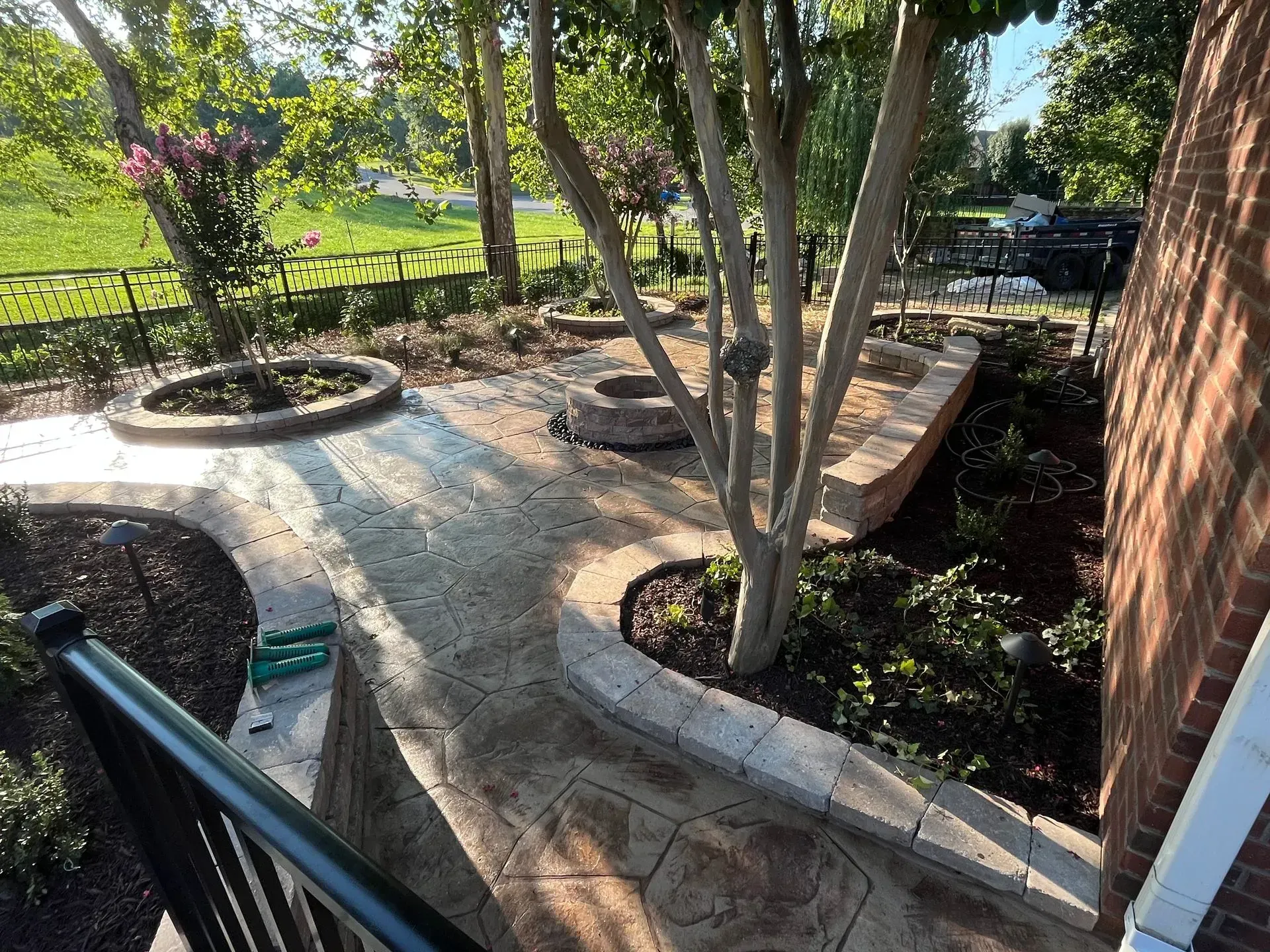 Pathway with landscaped beds and trees near a brick building.