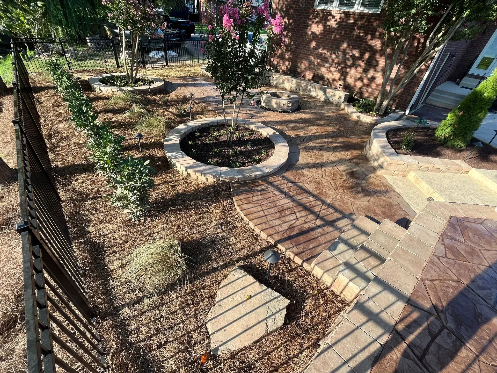 A backyard garden with brown mulch, a brick pathway, and various small trees.