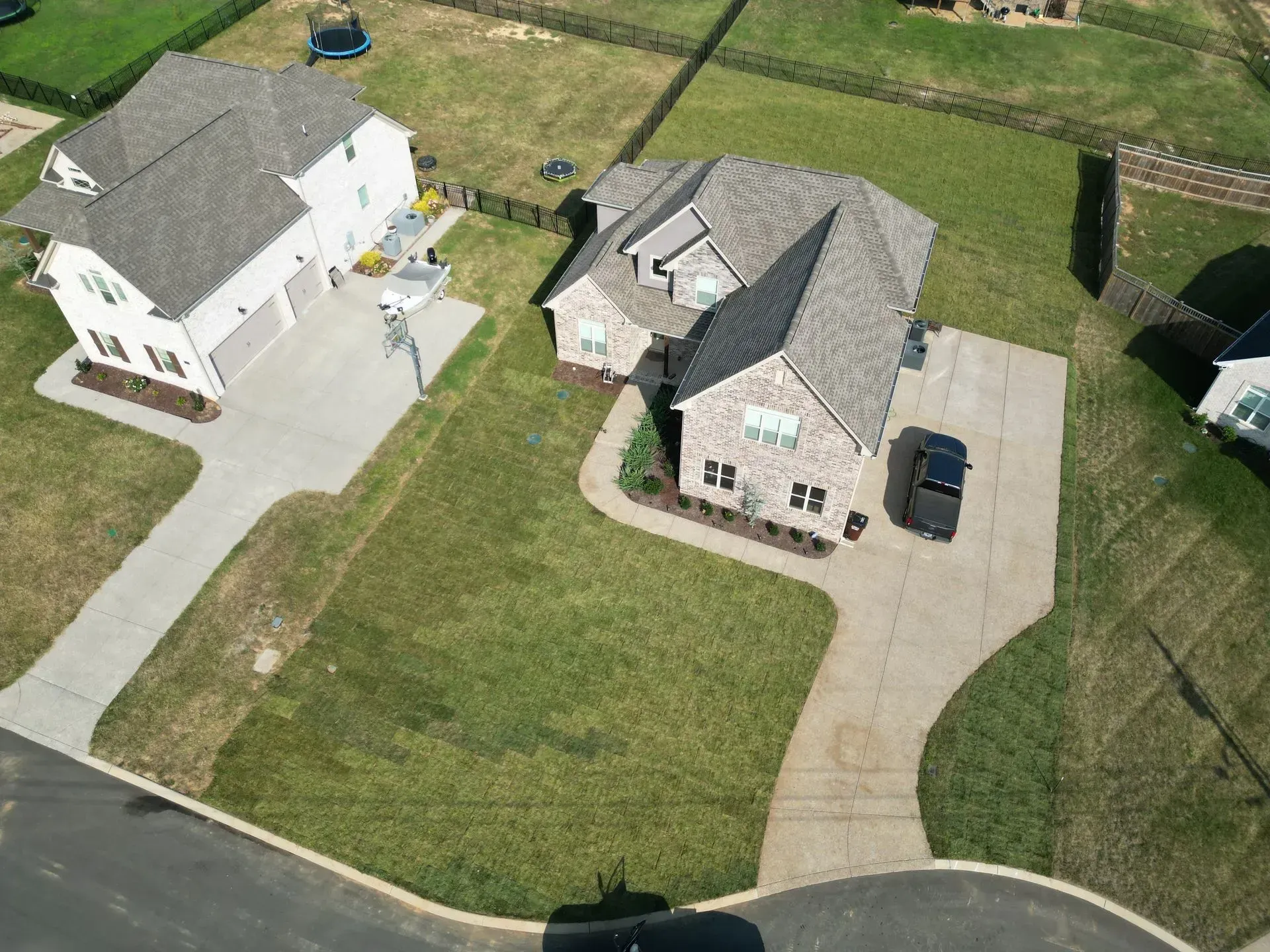 Aerial view of two houses. One brick, one white, with driveways and green lawns.