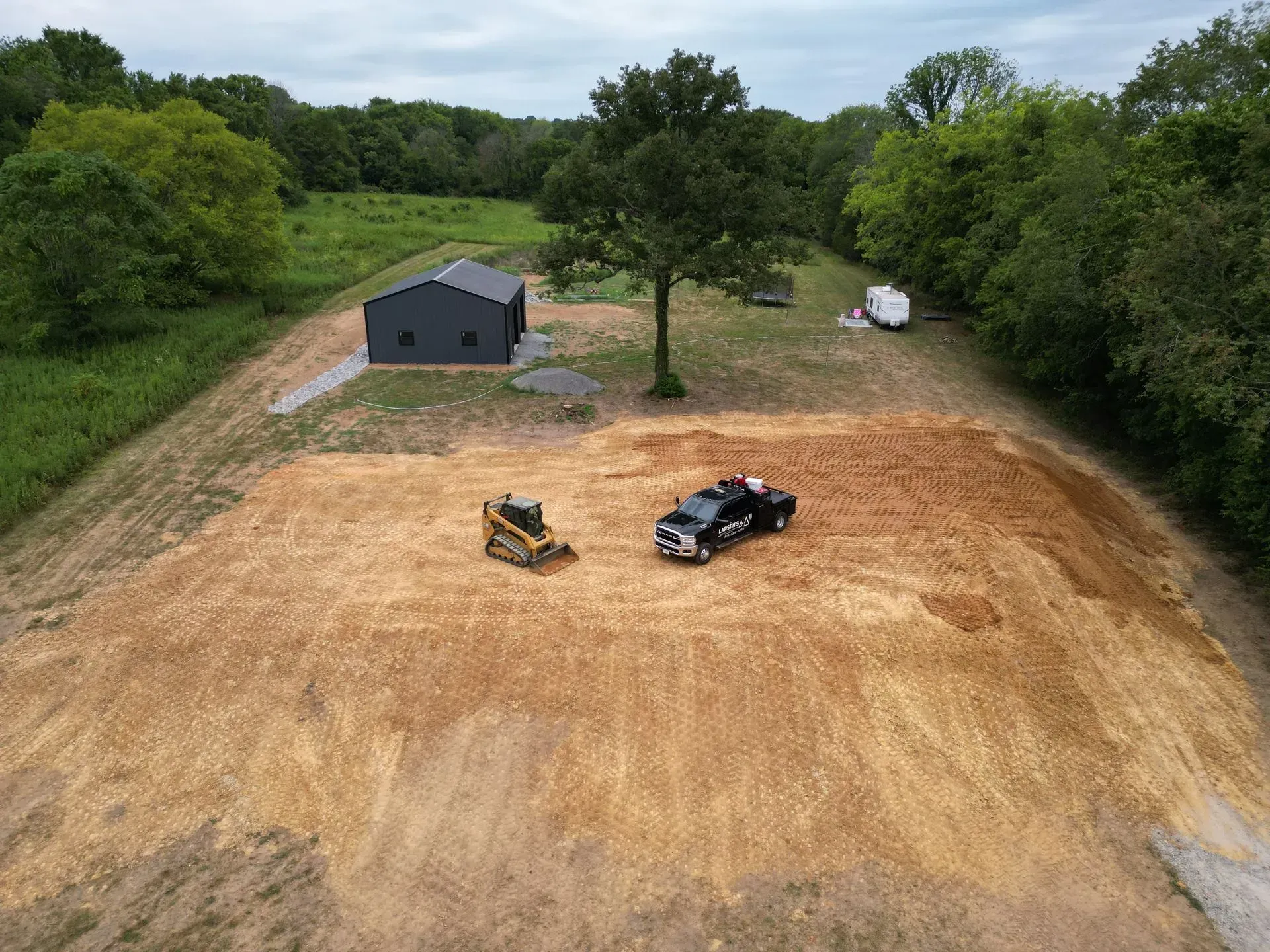 Aerial view: Construction site with a skid steer, truck, and a dark gray building.