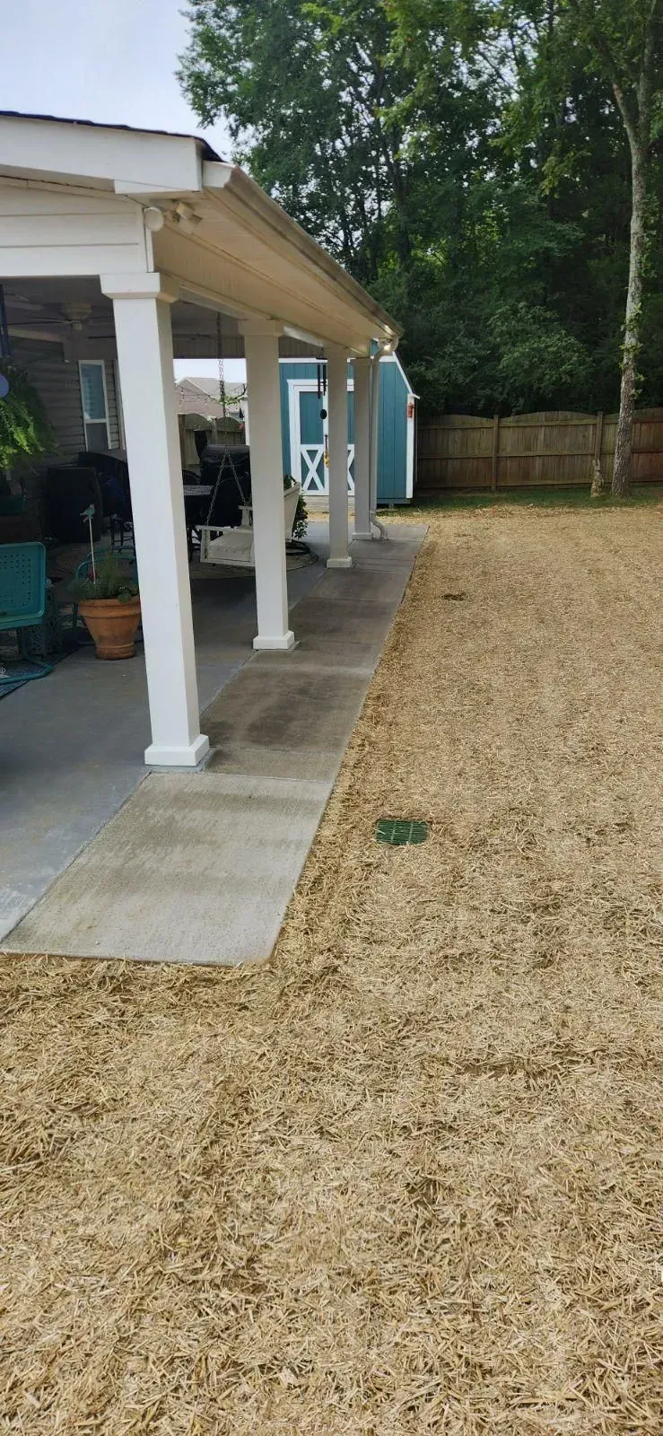 Backyard with a covered patio, gravel ground, blue shed, and trees.