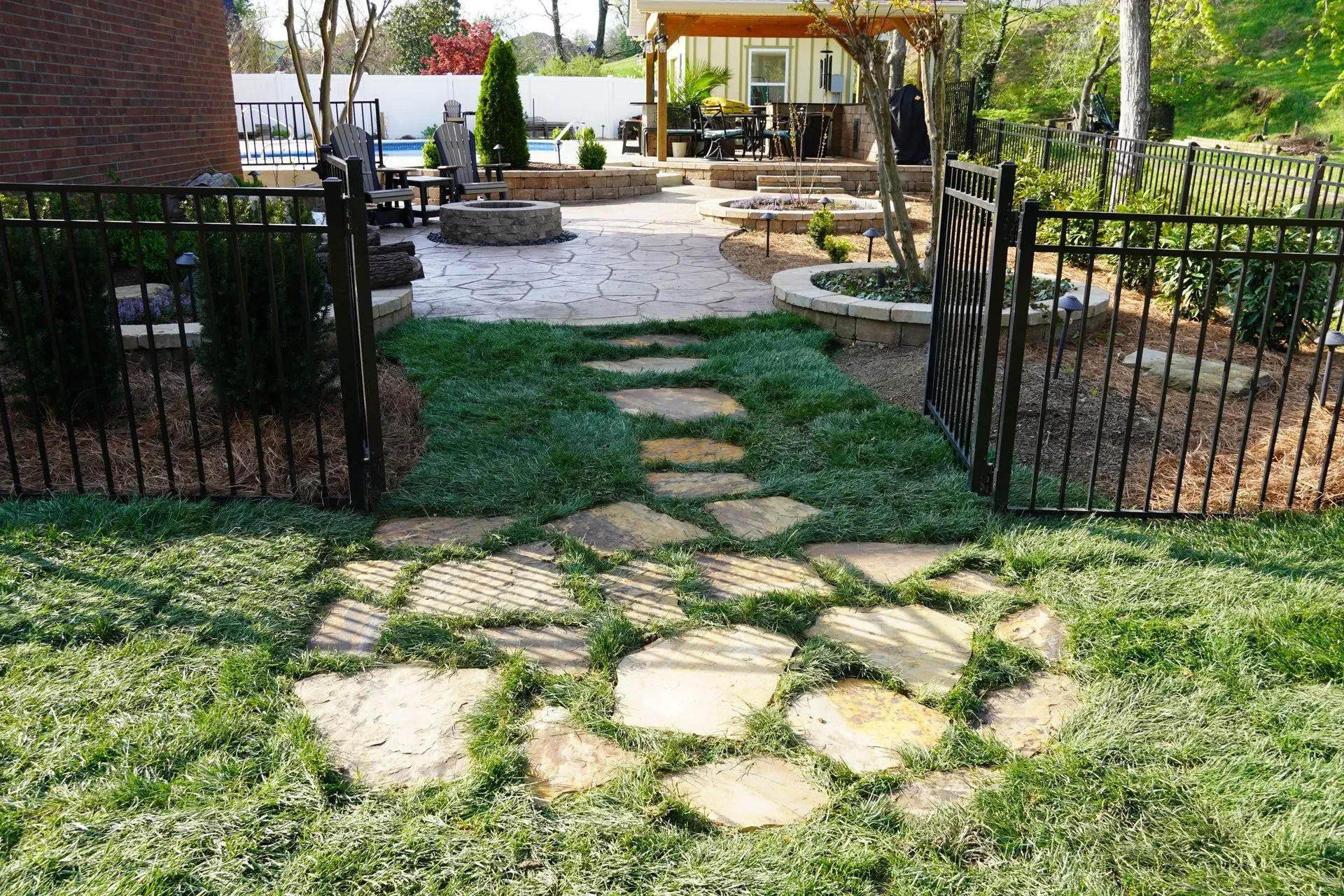 Stone pathway through green ground cover, leading to a backyard patio with a fire pit.