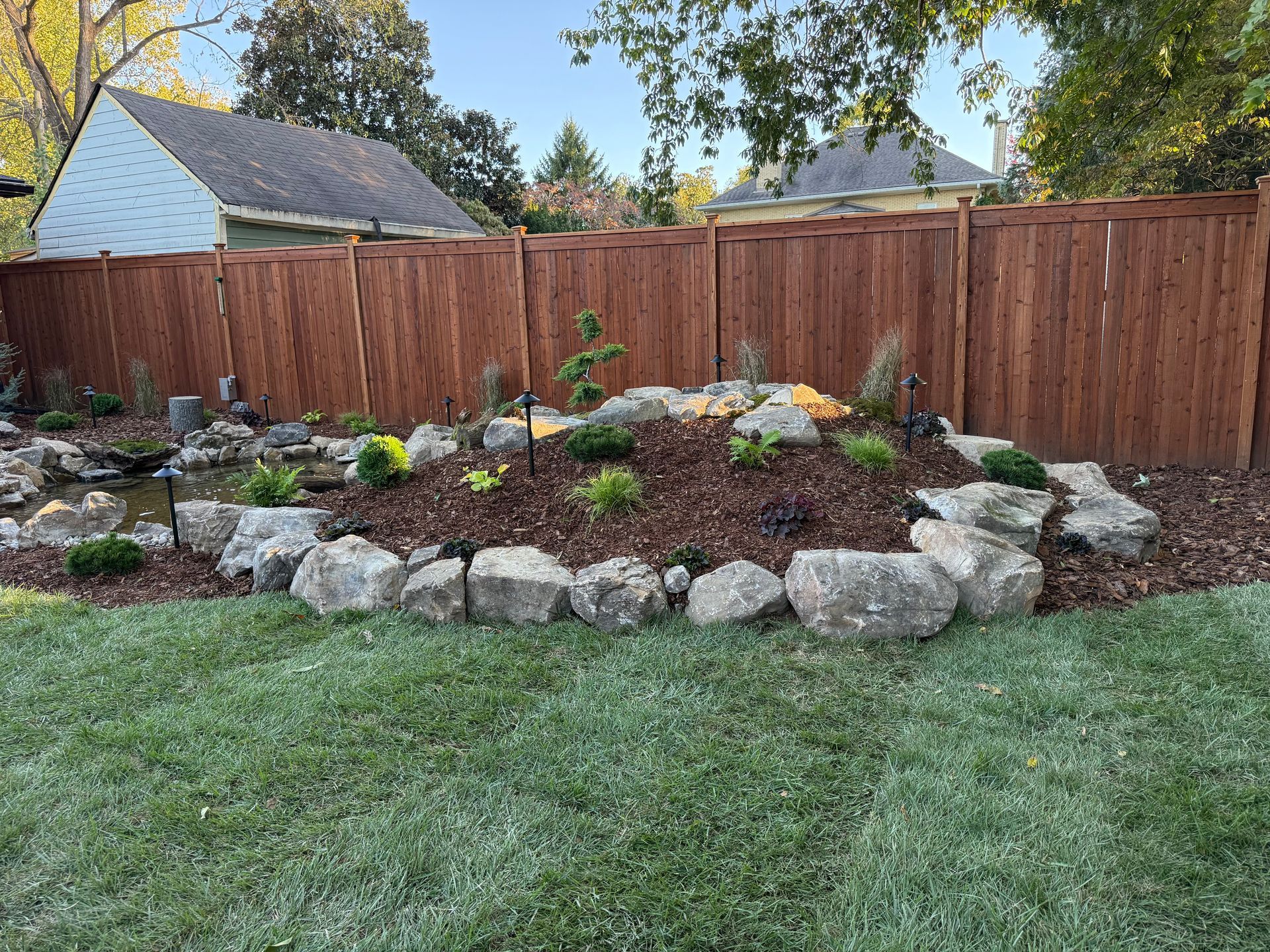 Backyard with a brown wooden fence, a rock garden, pond, and green lawn.