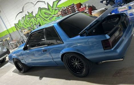 A blue mustang is parked in a garage with its trunk open.