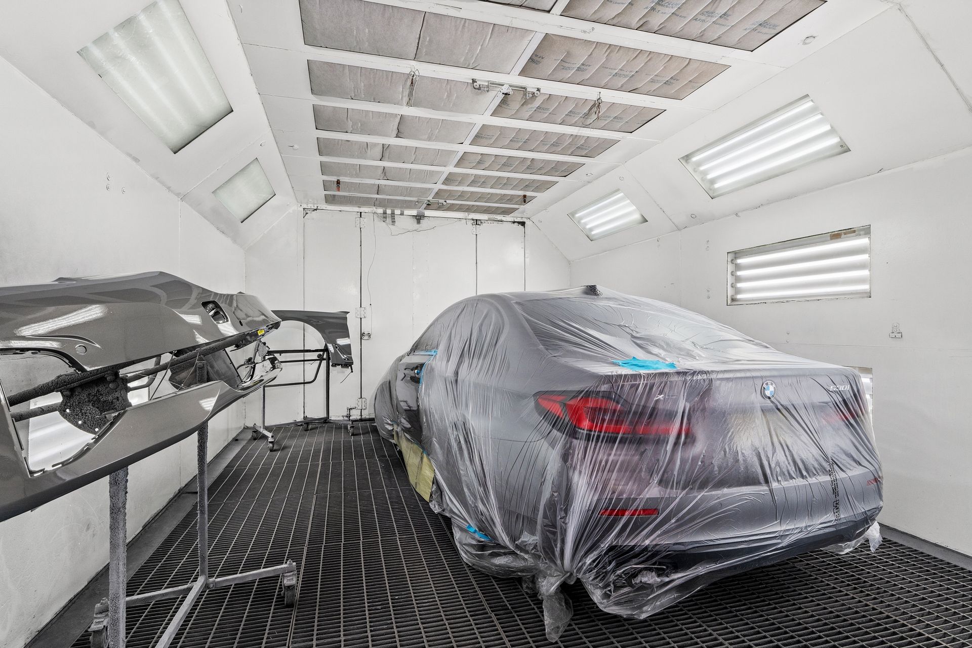 A car is covered in plastic while being painted in a paint booth