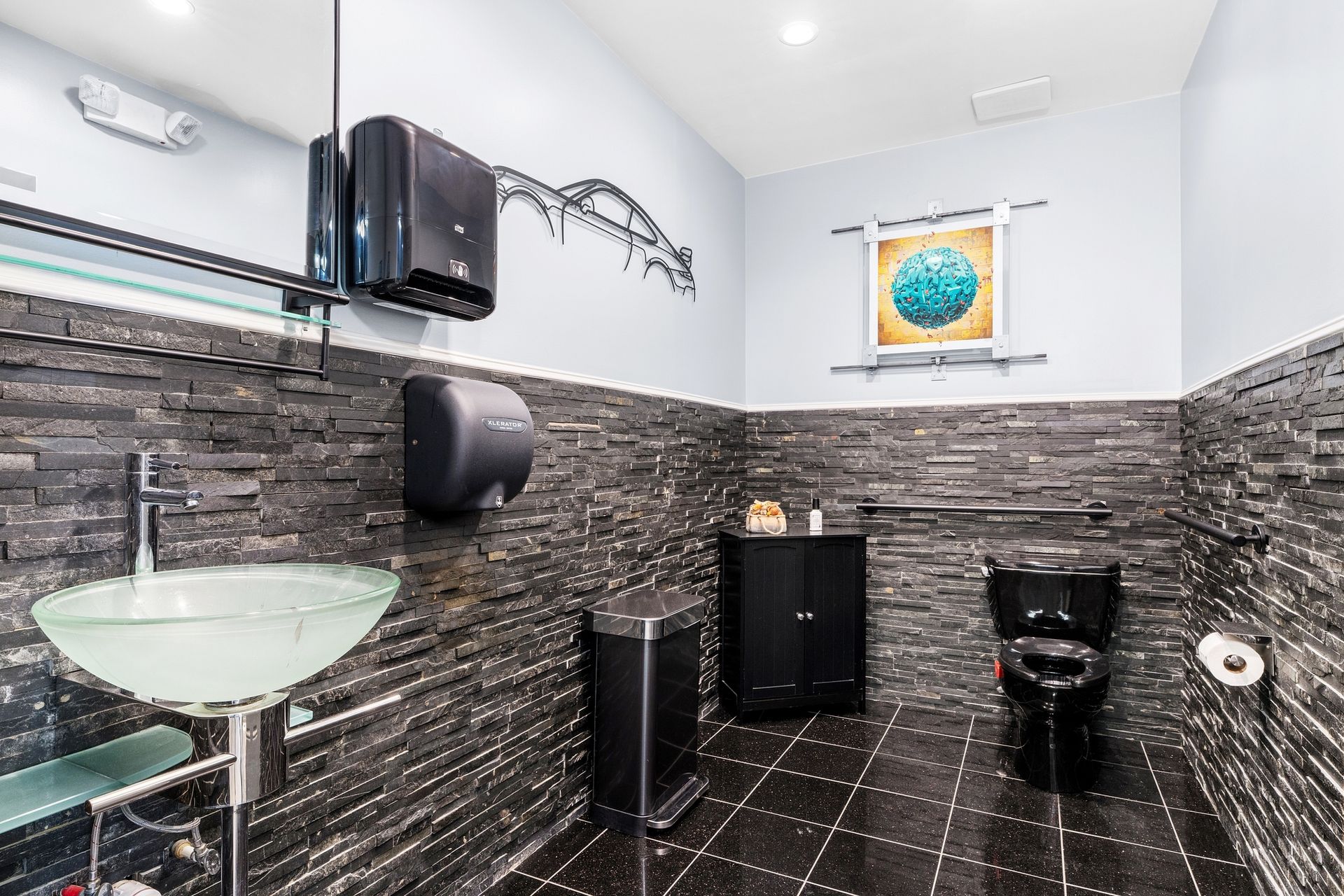 A bathroom with a sink, toilet, trash can and a picture on the wall