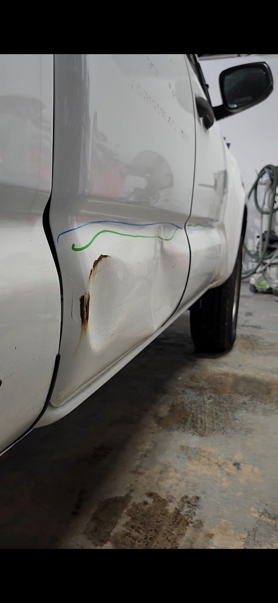 A white truck with a damaged side door is parked in a garage.