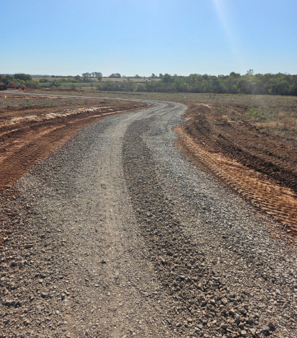 A gravel path curves through a construction site with excavated red dirt under a clear blue sky.