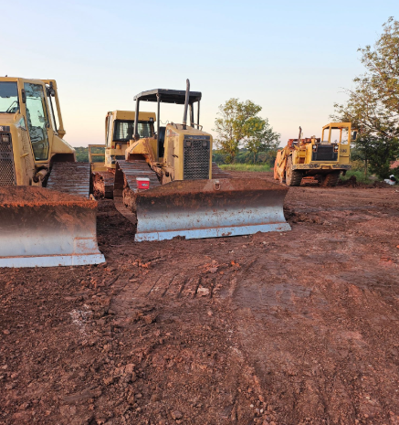 Three yellow construction bulldozers parked on a brown dirt field under a clear sky.