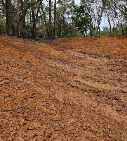 Freshly cleared red clay ground with tire tracks leading toward a line of trees in the background.