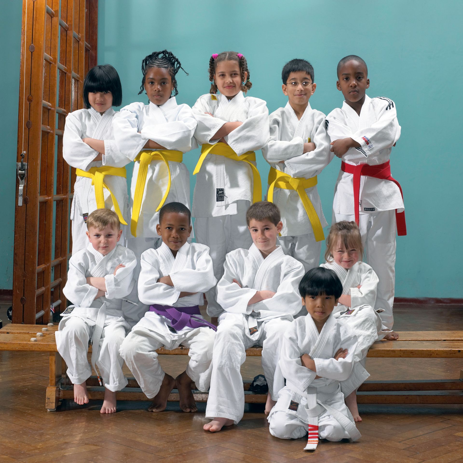 Children in white martial arts uniforms with colored belts posing on a stage