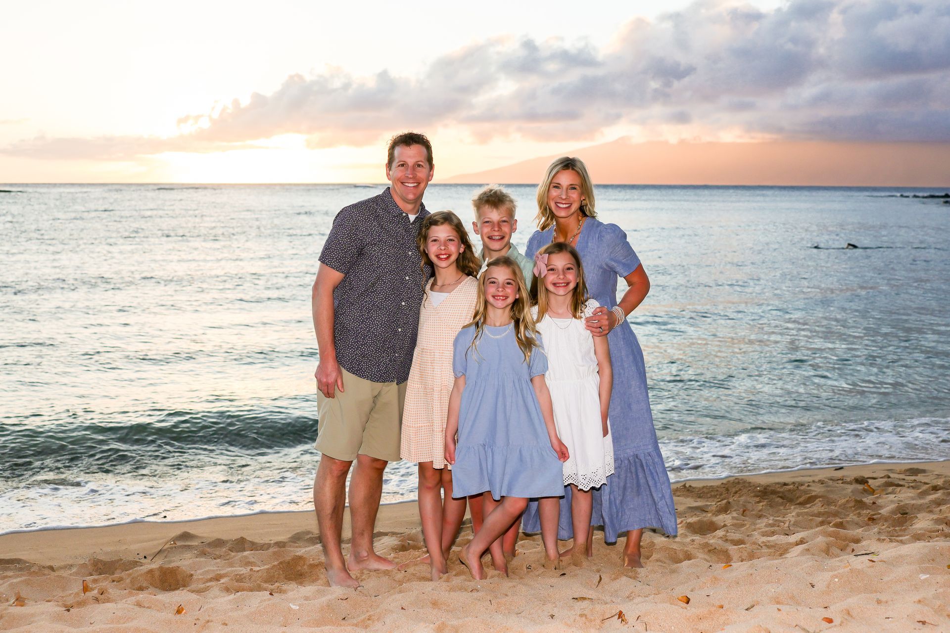 Family of six on beach at sunset, posing for photo.