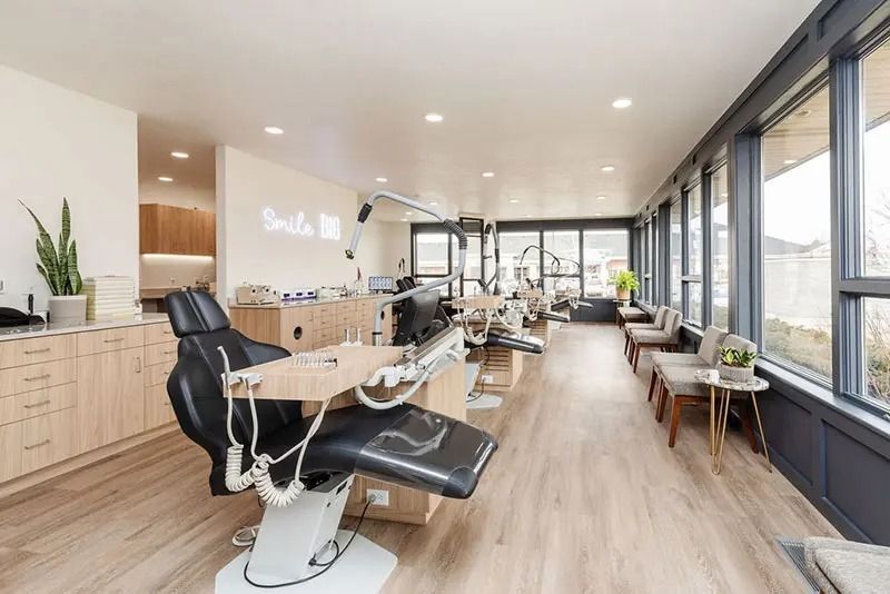 Modern dental office interior, light wood floors, dental chairs, large windows, waiting area.