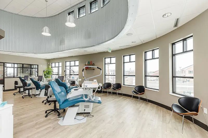 Dental office interior with blue chairs and equipment, natural light from windows, and curved wall.