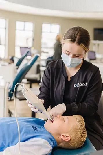 Dentist scanning a child's mouth with a handheld device in a dental office. The child is lying down.